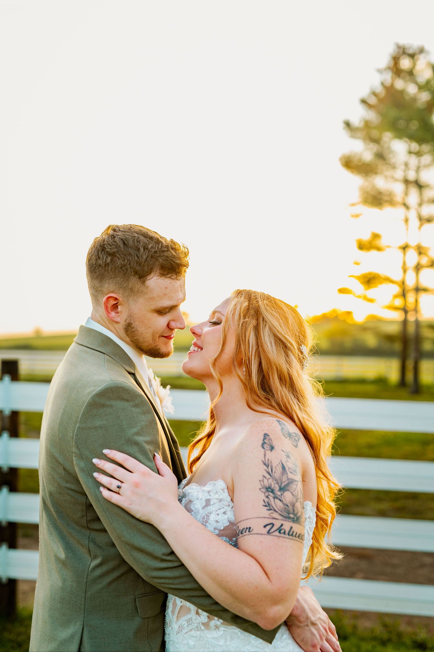 Intimate sunset wedding portrait against a rustic fence with golden light filtering through trees.
