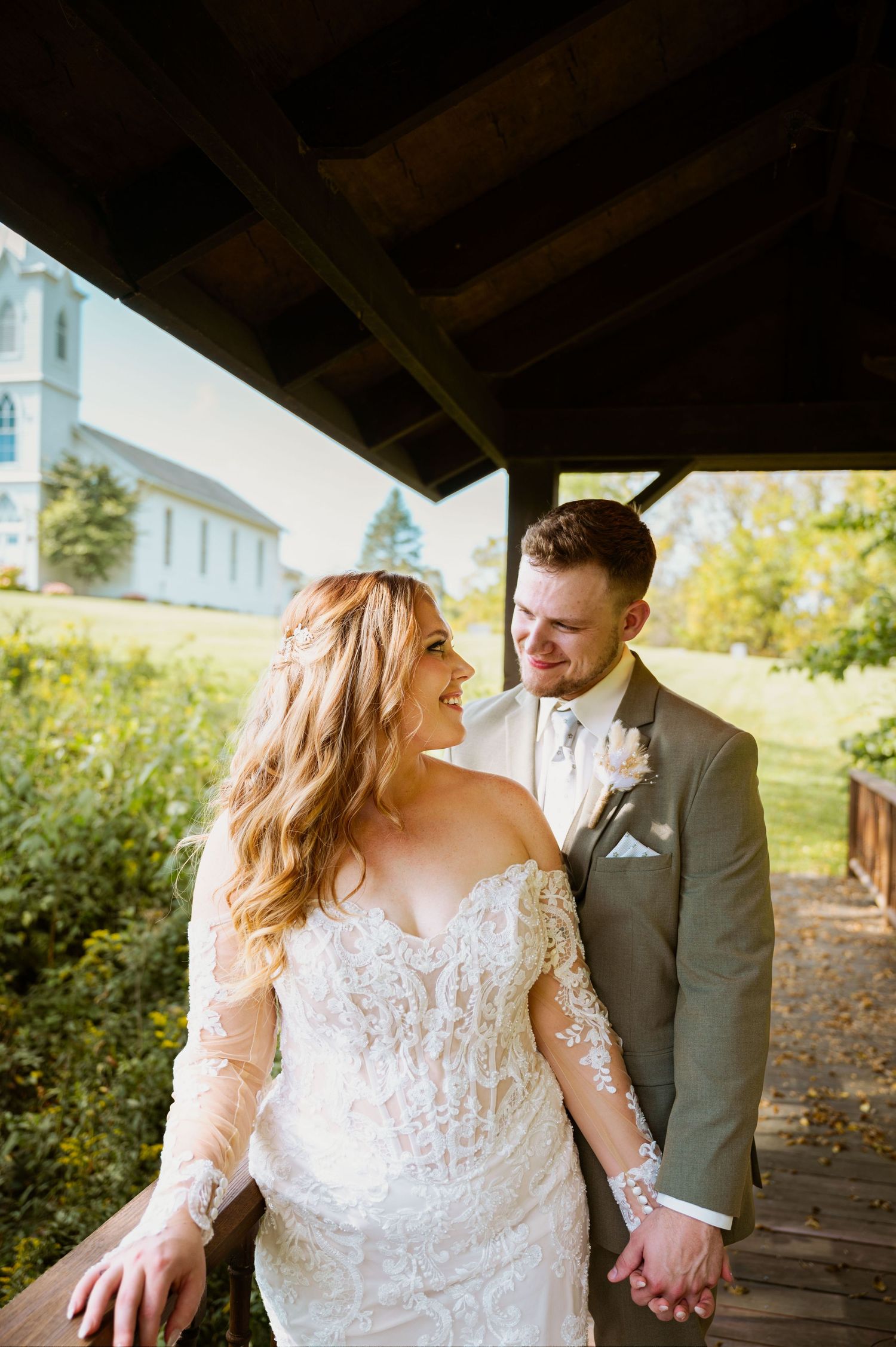 A romantic wedding couple shares intimate moments under a covered walkway with a church visible in background.