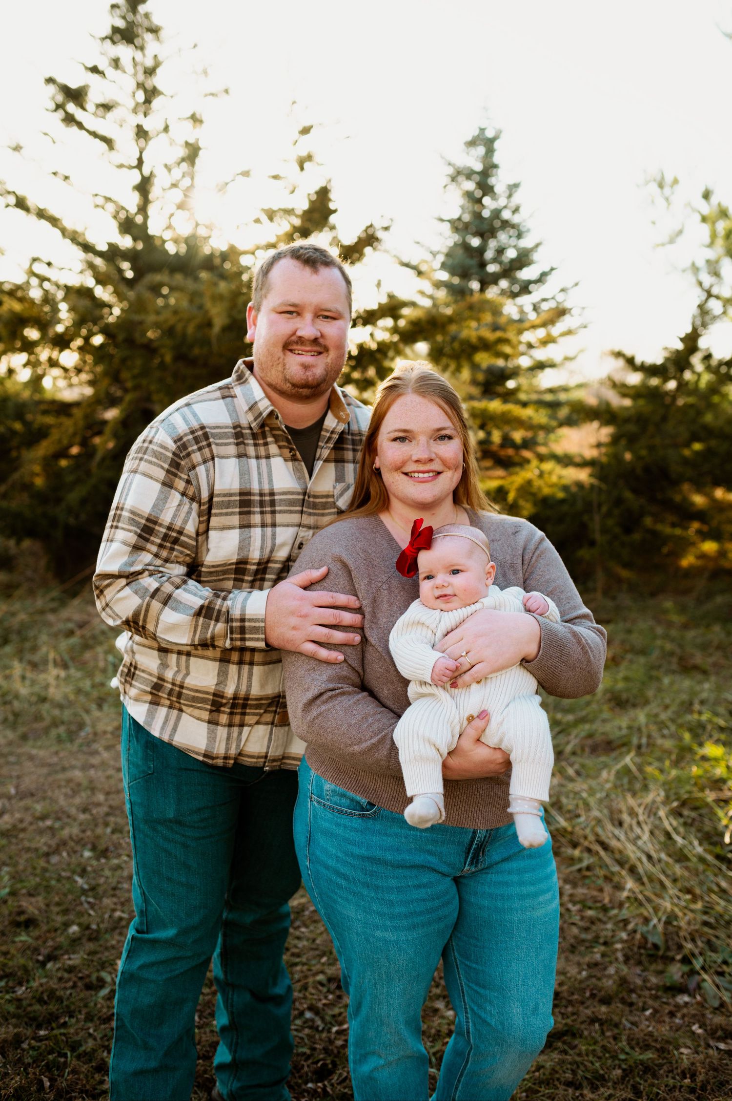 A family in matching plaid and denim poses together outdoors during golden hour sunset.
