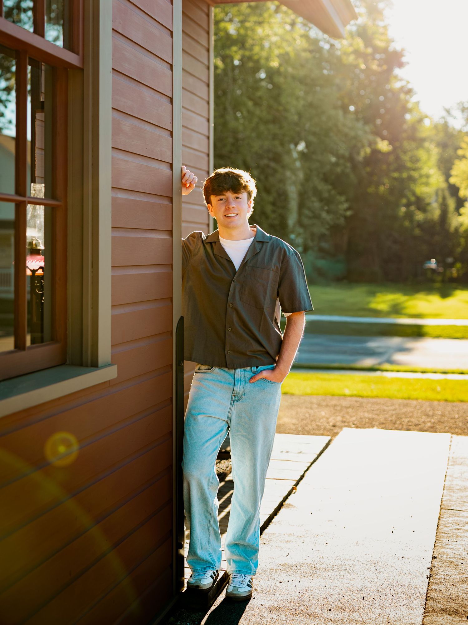 A person in casual attire leans against a brown building exterior during golden hour sunlight.