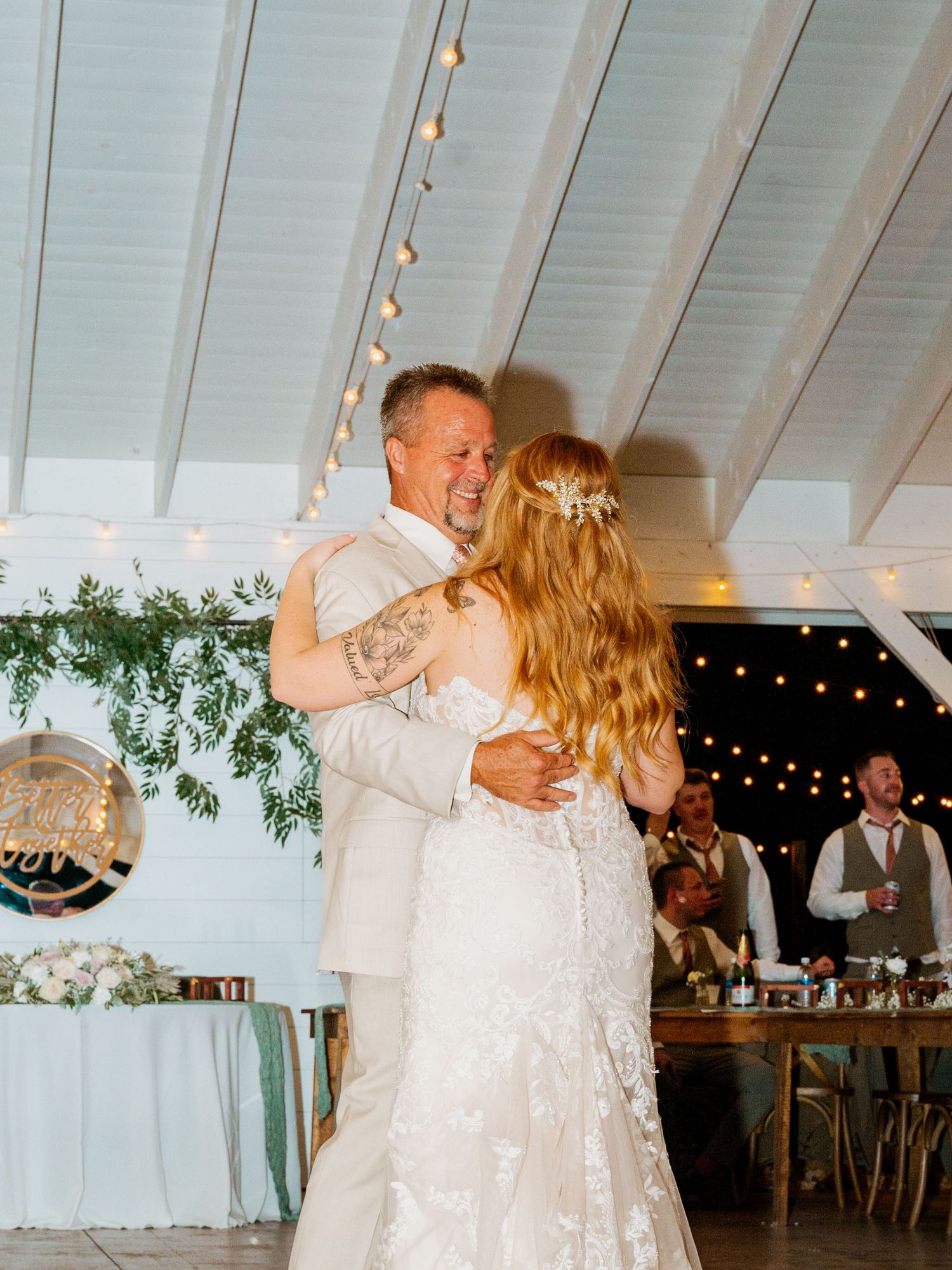 Emotional dance moment under white rafters with string lights creating an intimate reception atmosphere.