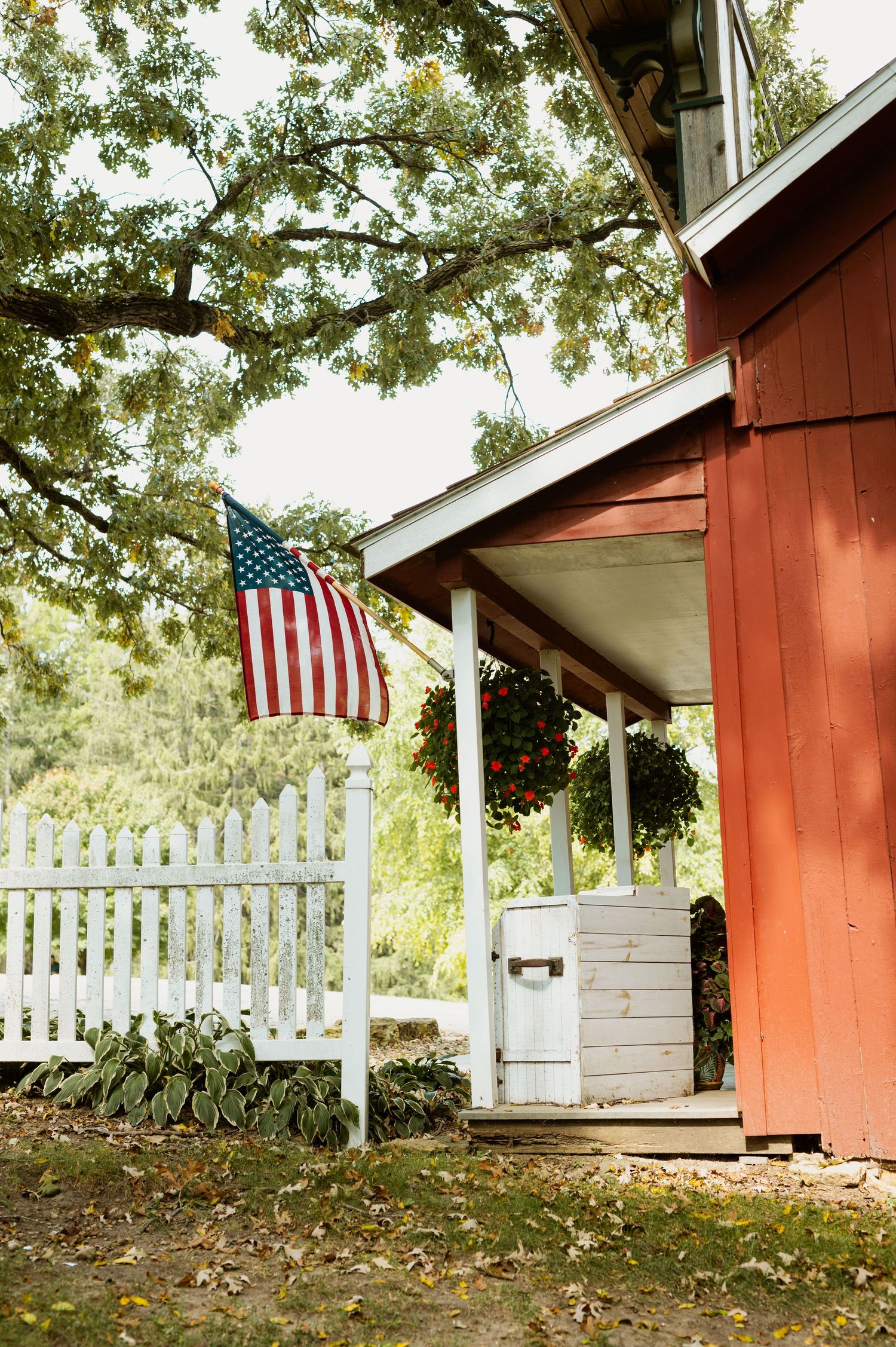 Red barn building with white picket fence and American flag displayed outside.