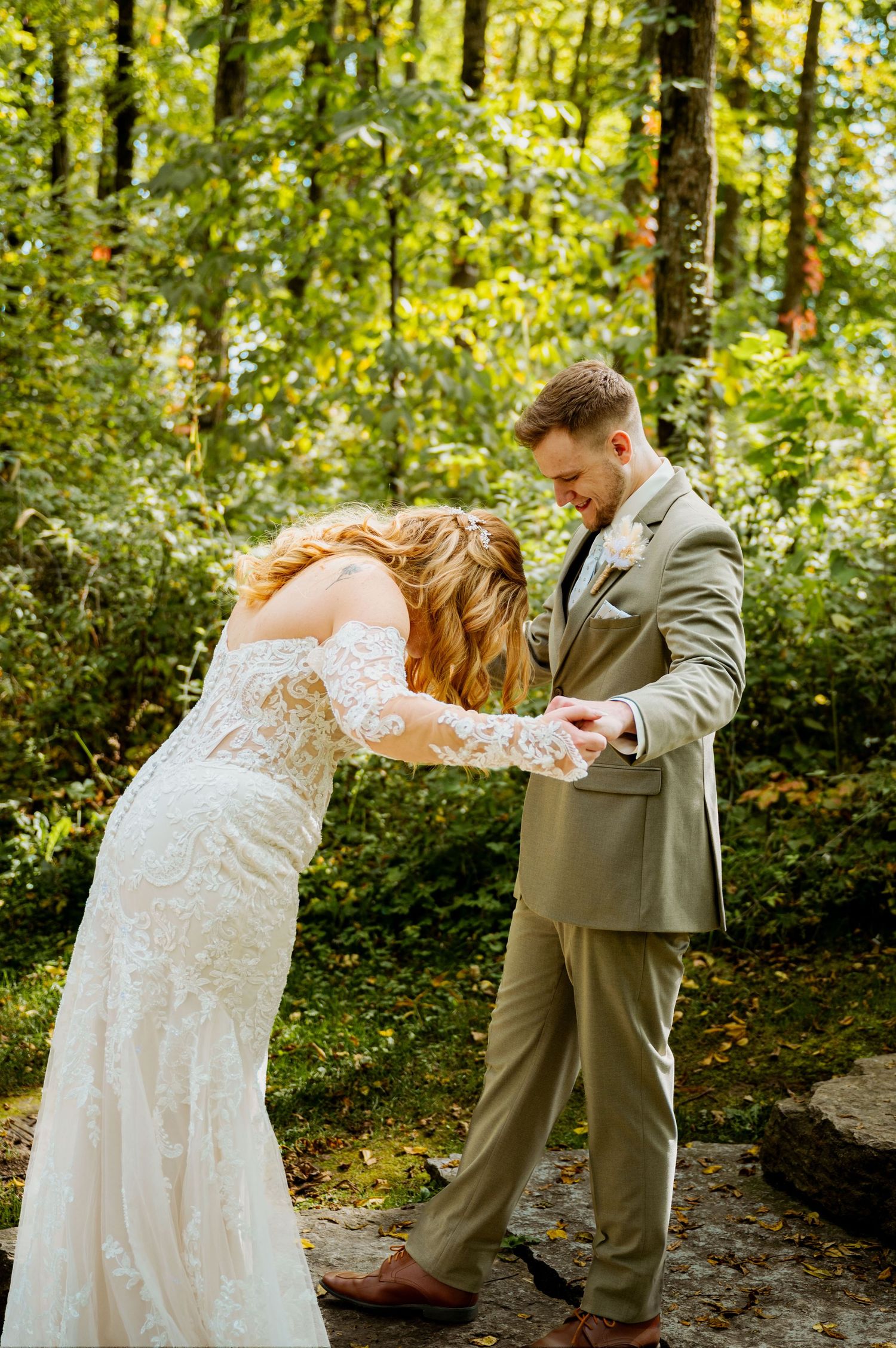 Bride and groom sharing playful dance moves during their first look in a wooded setting.