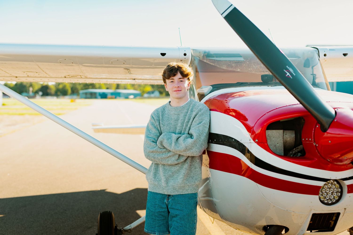 A red and white small aircraft parked on an airfield with someone standing beside it.