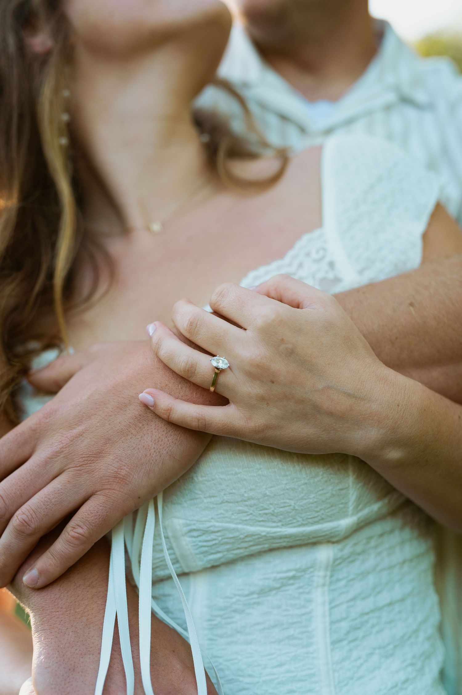 Close-up of hands with engagement ring embracing in romantic outdoor setting.