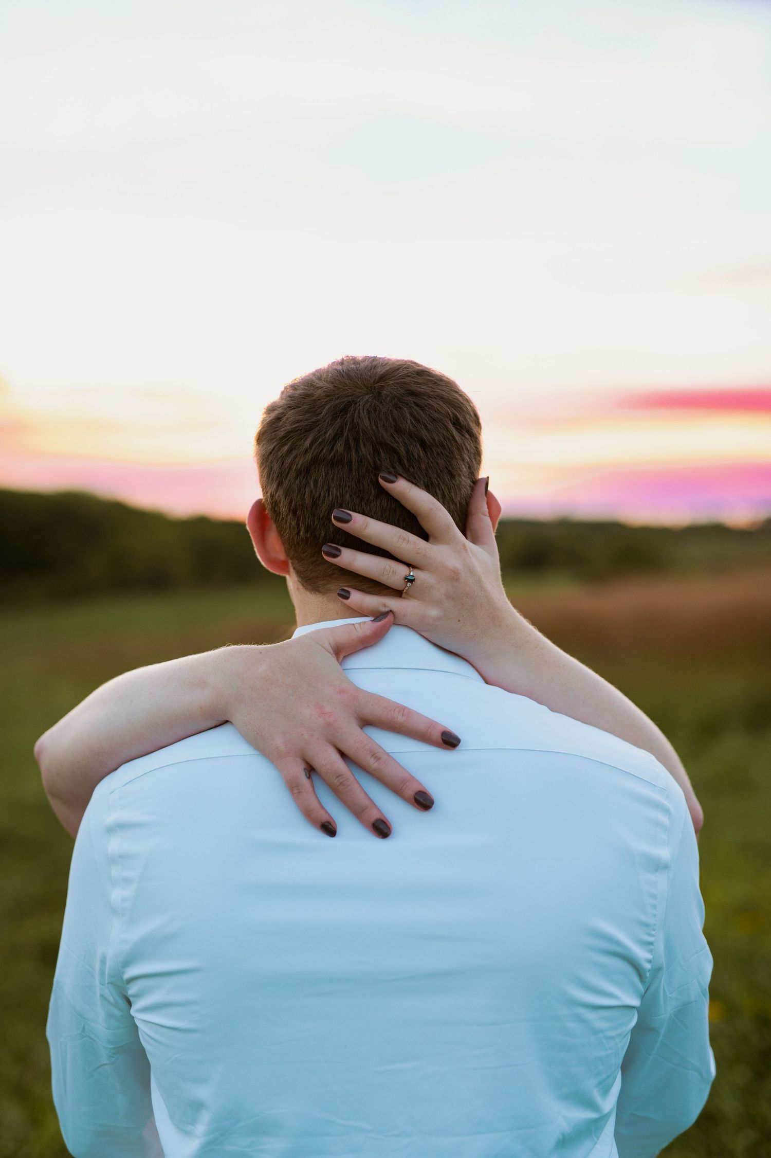 Intimate embrace captured from behind showing hands wrapped around shoulders during golden hour.
