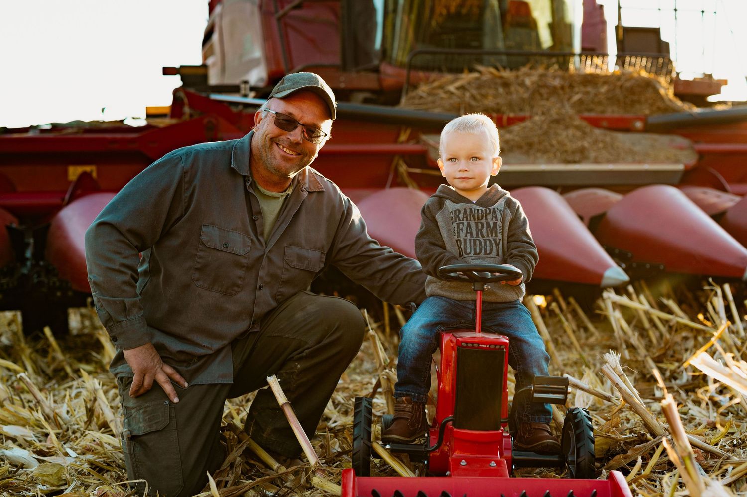 A red toy wagon sits among dried corn stalks during an autumn harvest scene.