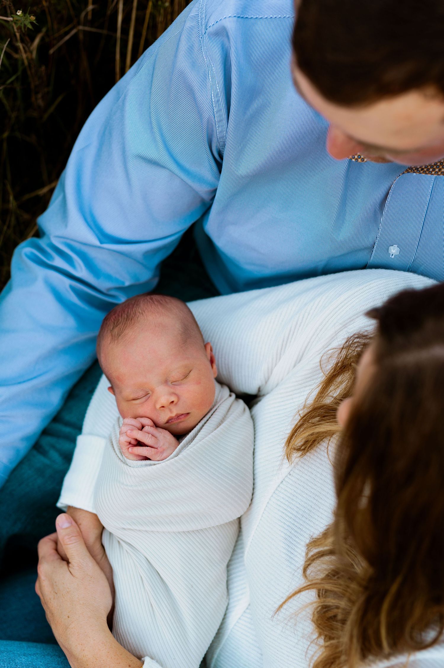 Newborn baby wrapped in white blanket being cradled during intimate family moment.