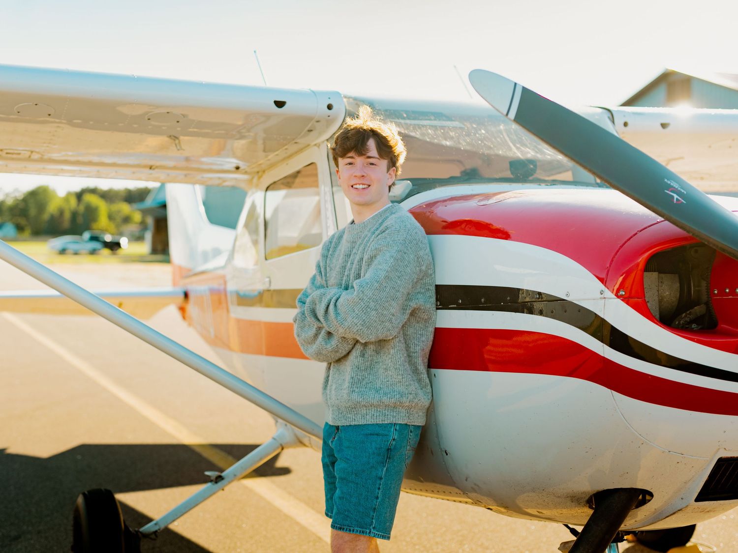 A small white and red private aircraft parked on a sunny airfield with someone inspecting its exterior.