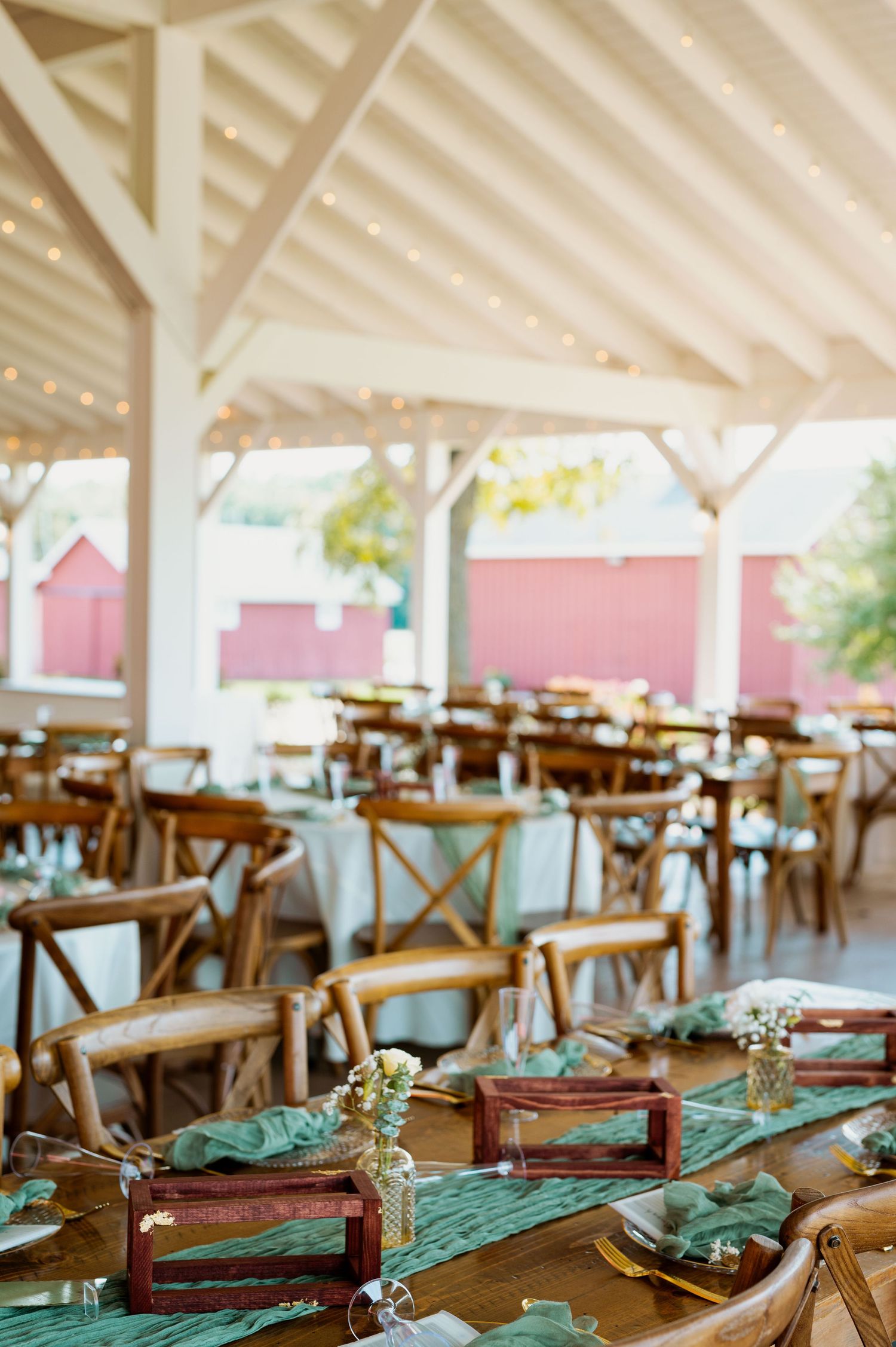 Rustic wedding reception venue with wooden chairs and teal table runners in an open-air pavilion.