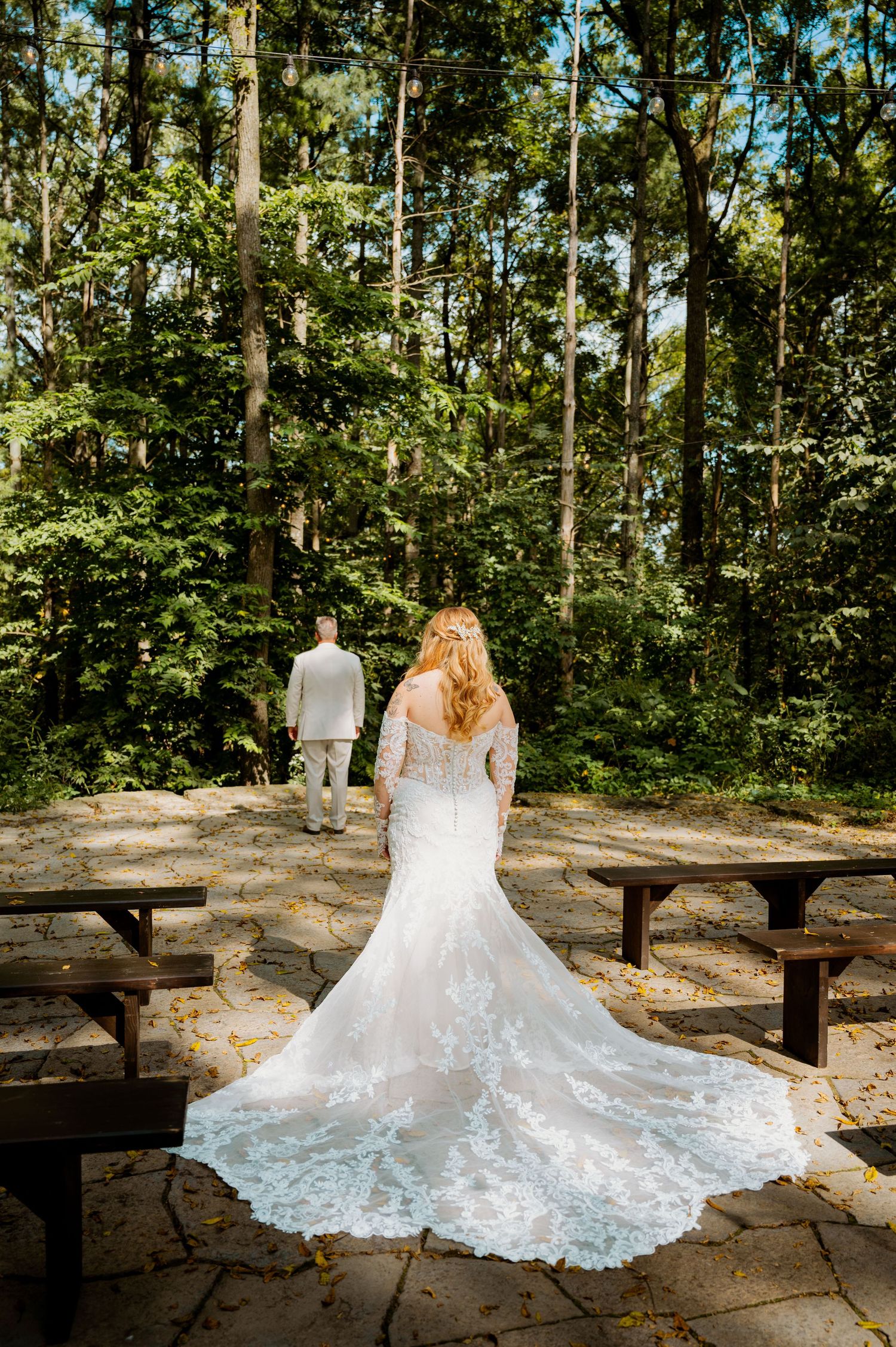 Elegant lace wedding dress train spread across a stone patio surrounded by lush green forest scenery.