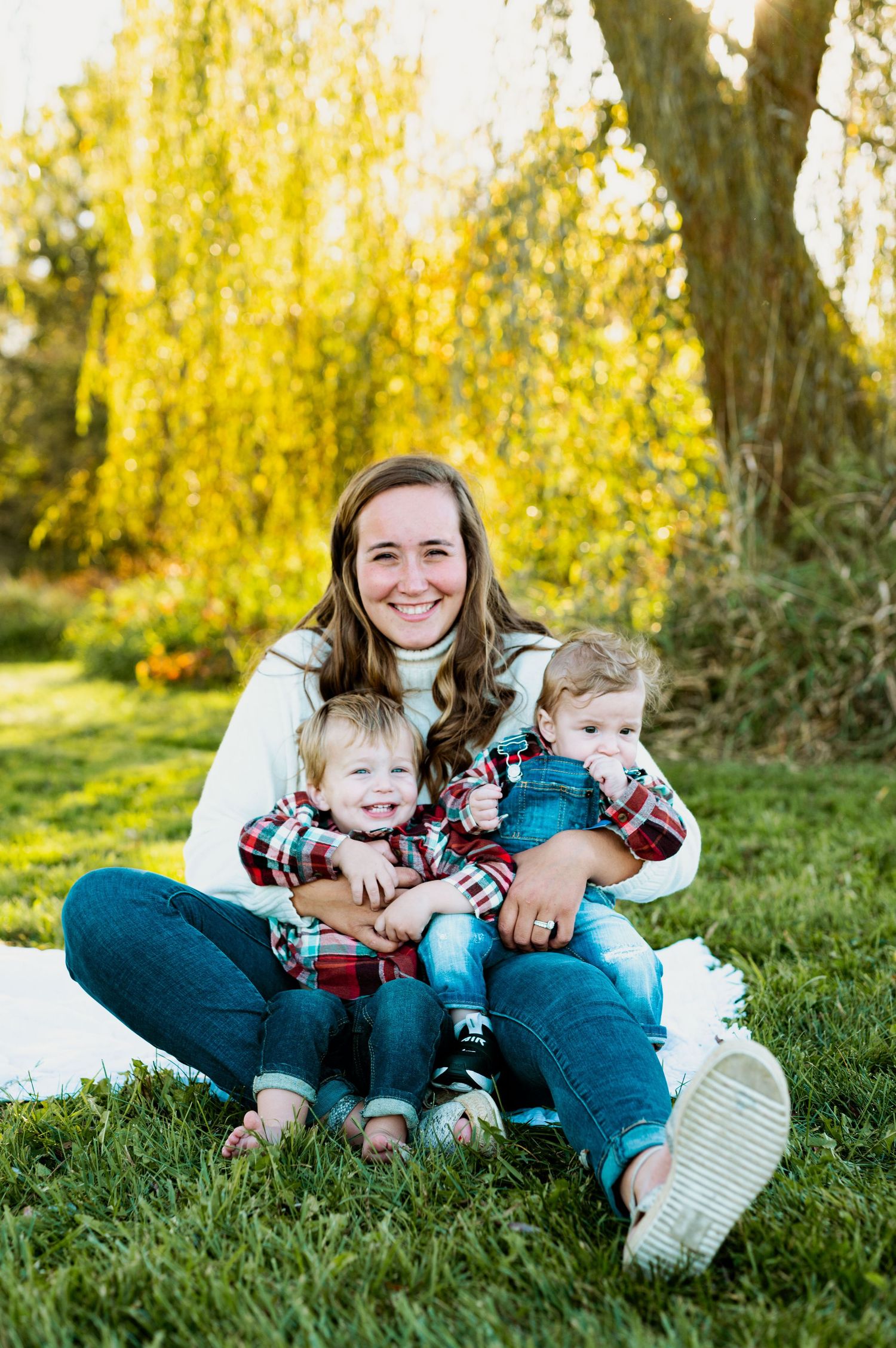 Family sits together on grass with beautiful yellow autumn foliage in background during outdoor portrait session.