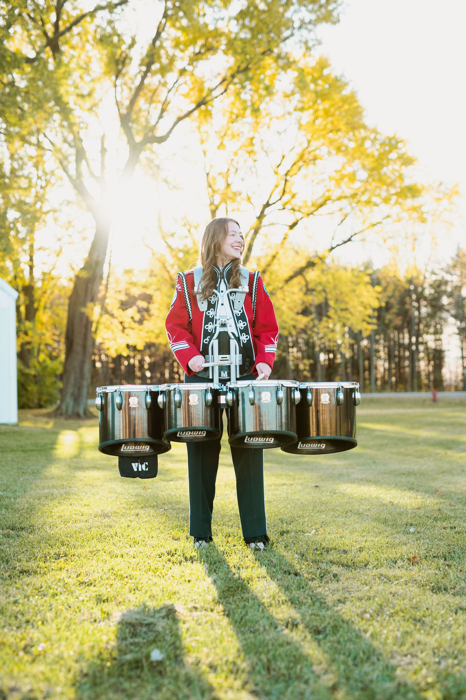 Percussion player in marching band uniform poses with drums at sunset.