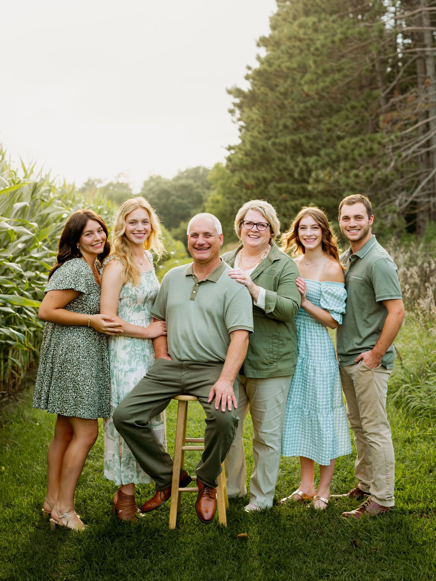 A group wearing coordinated sage green and blue outfits poses together outdoors in a natural setting.