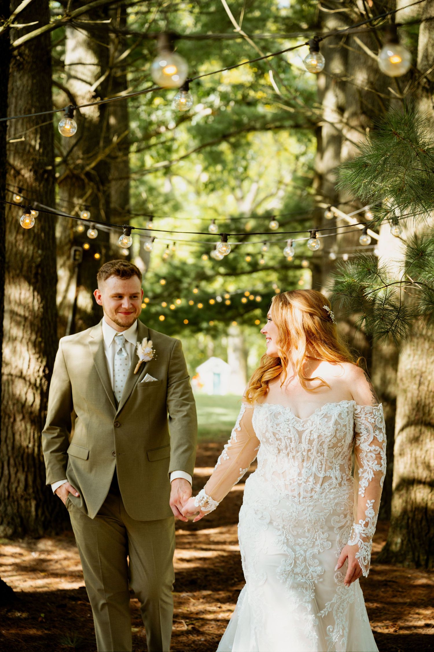 A couple shares intimate moments under string lights in a pine forest setting.