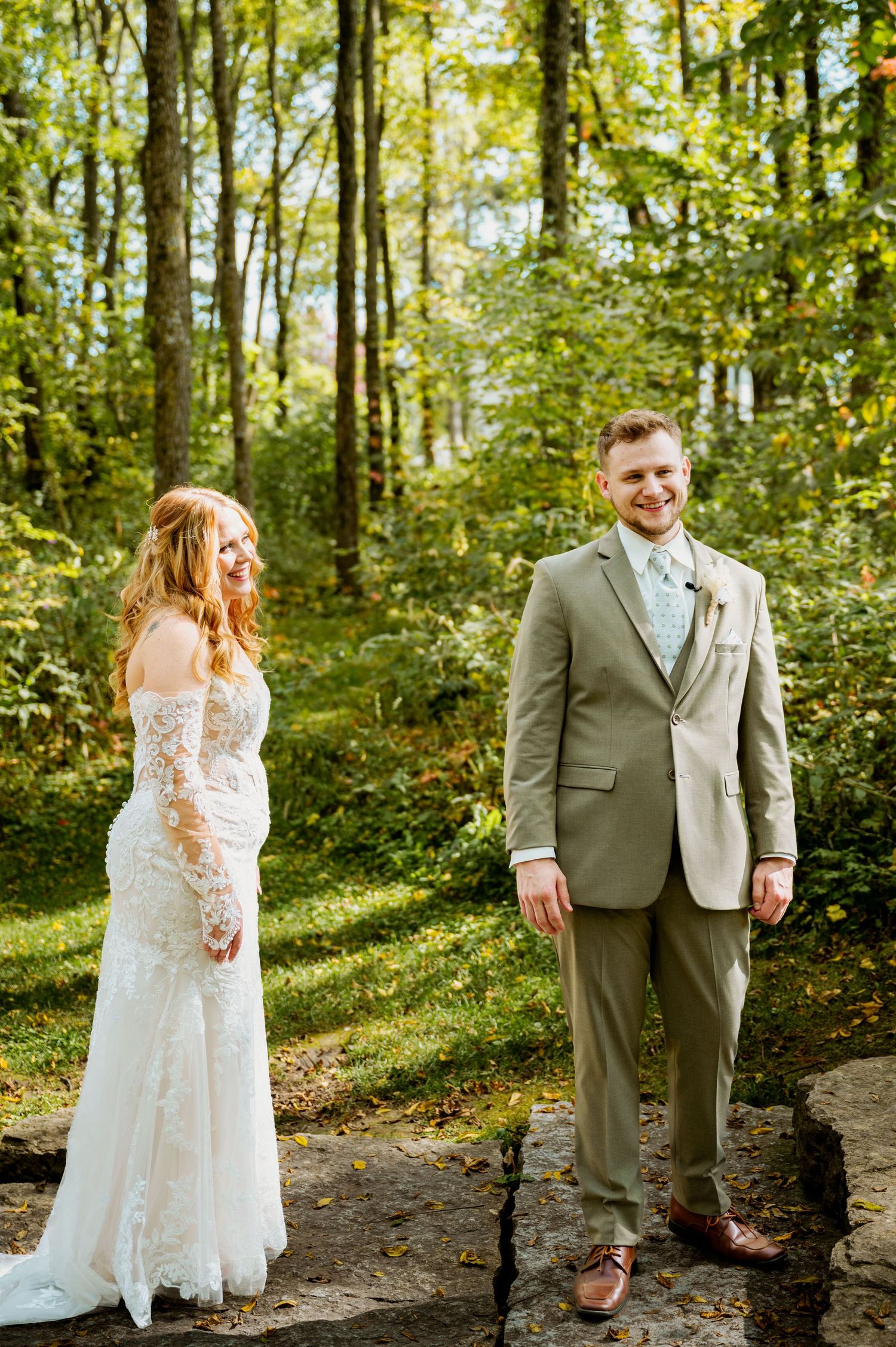 A couple shares a romantic moment in a sunlit forest wearing wedding attire.