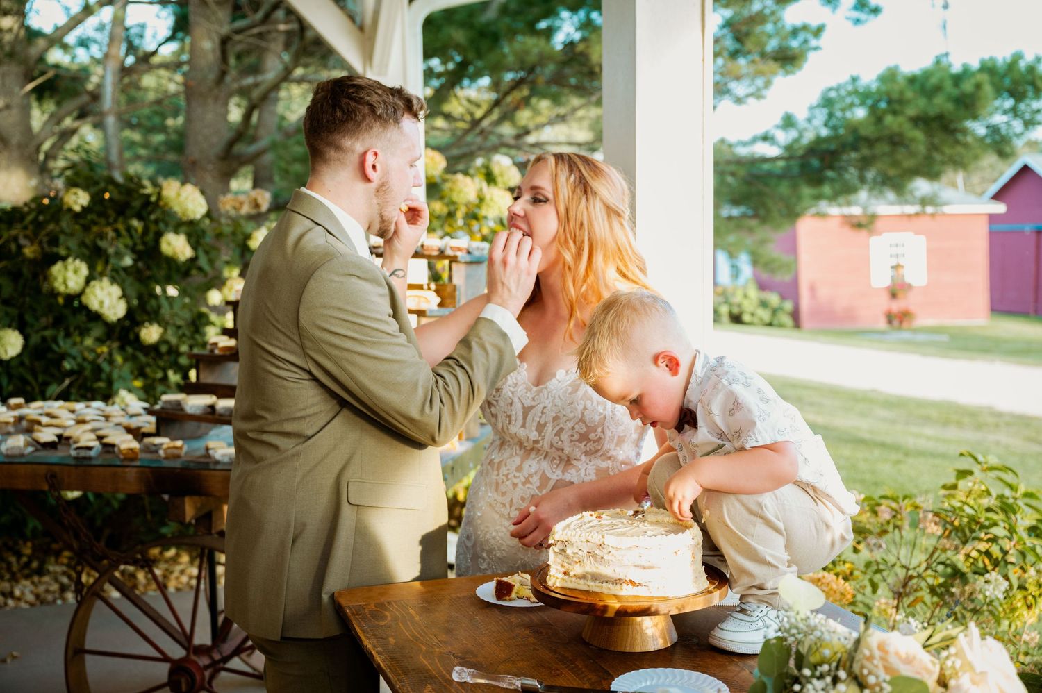 A joyful wedding cake cutting moment on a covered porch with yellow roses in the background.