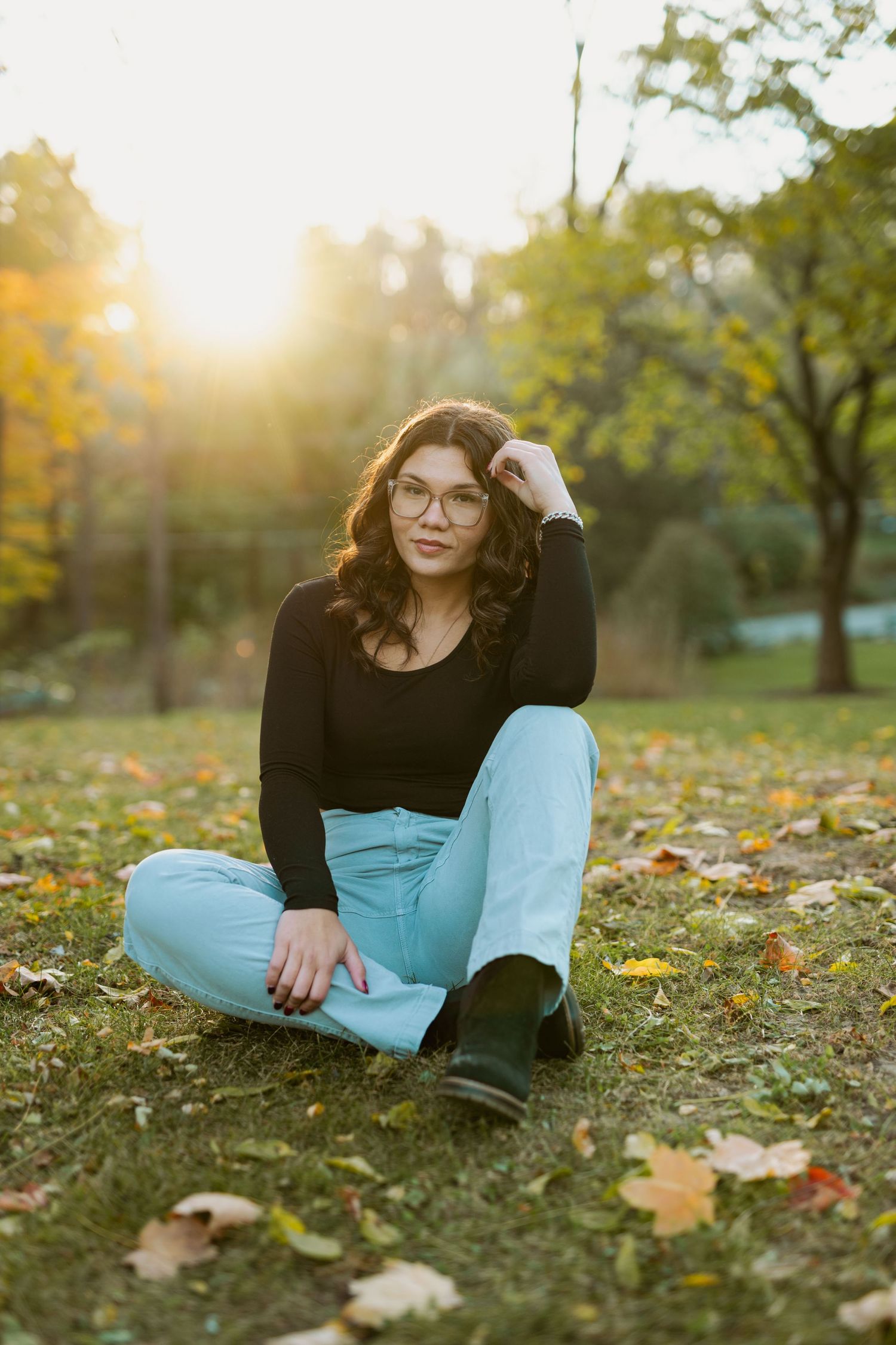Casual outdoor portrait session among fallen autumn leaves with soft evening light.