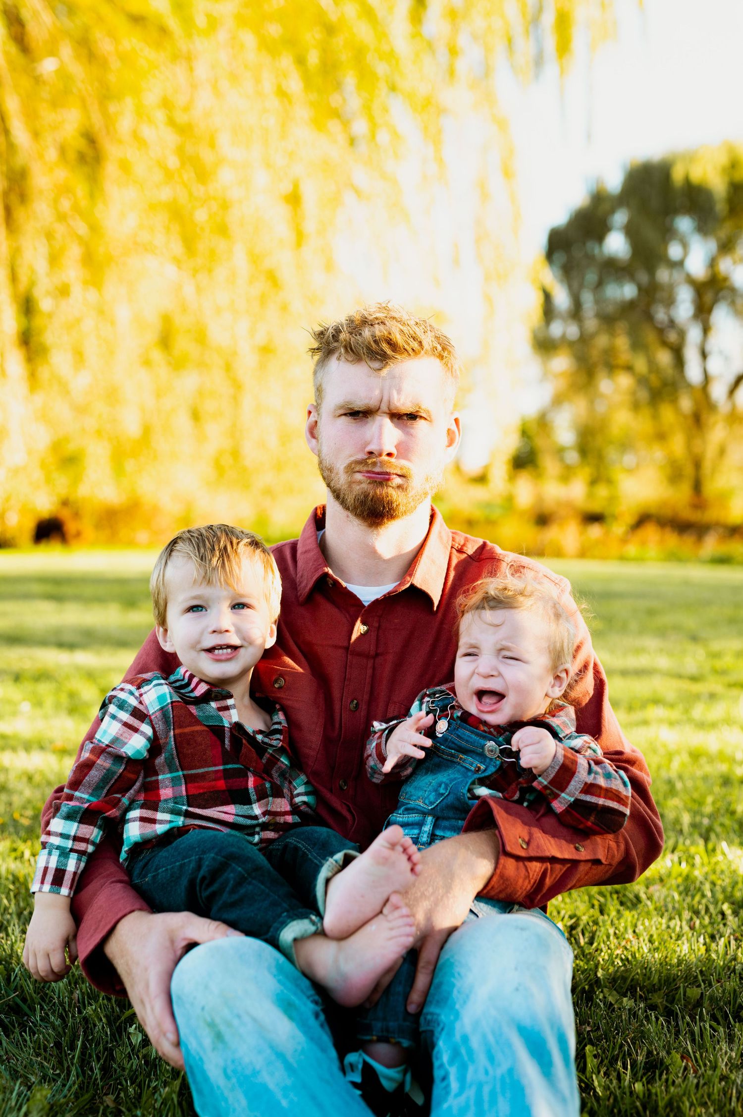 A sunny outdoor family portrait with matching plaid shirts against golden willow trees in the background.