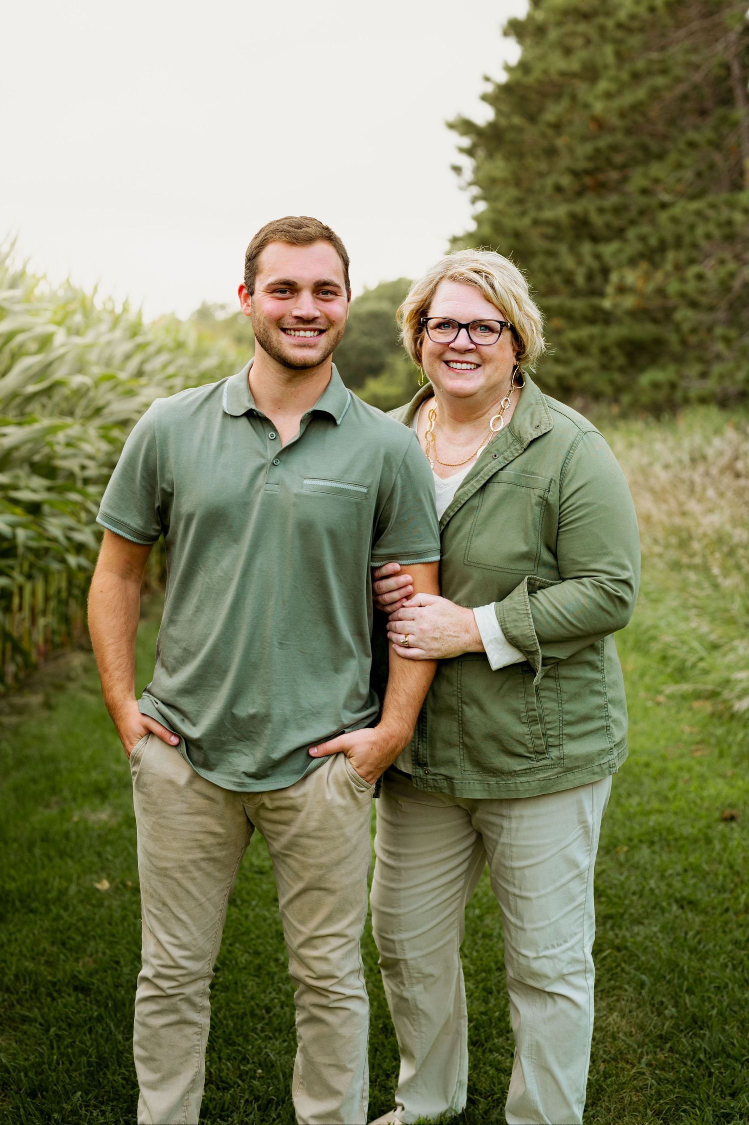 Two people wearing matching green polo shirts and khaki pants stand together on grass outdoors.