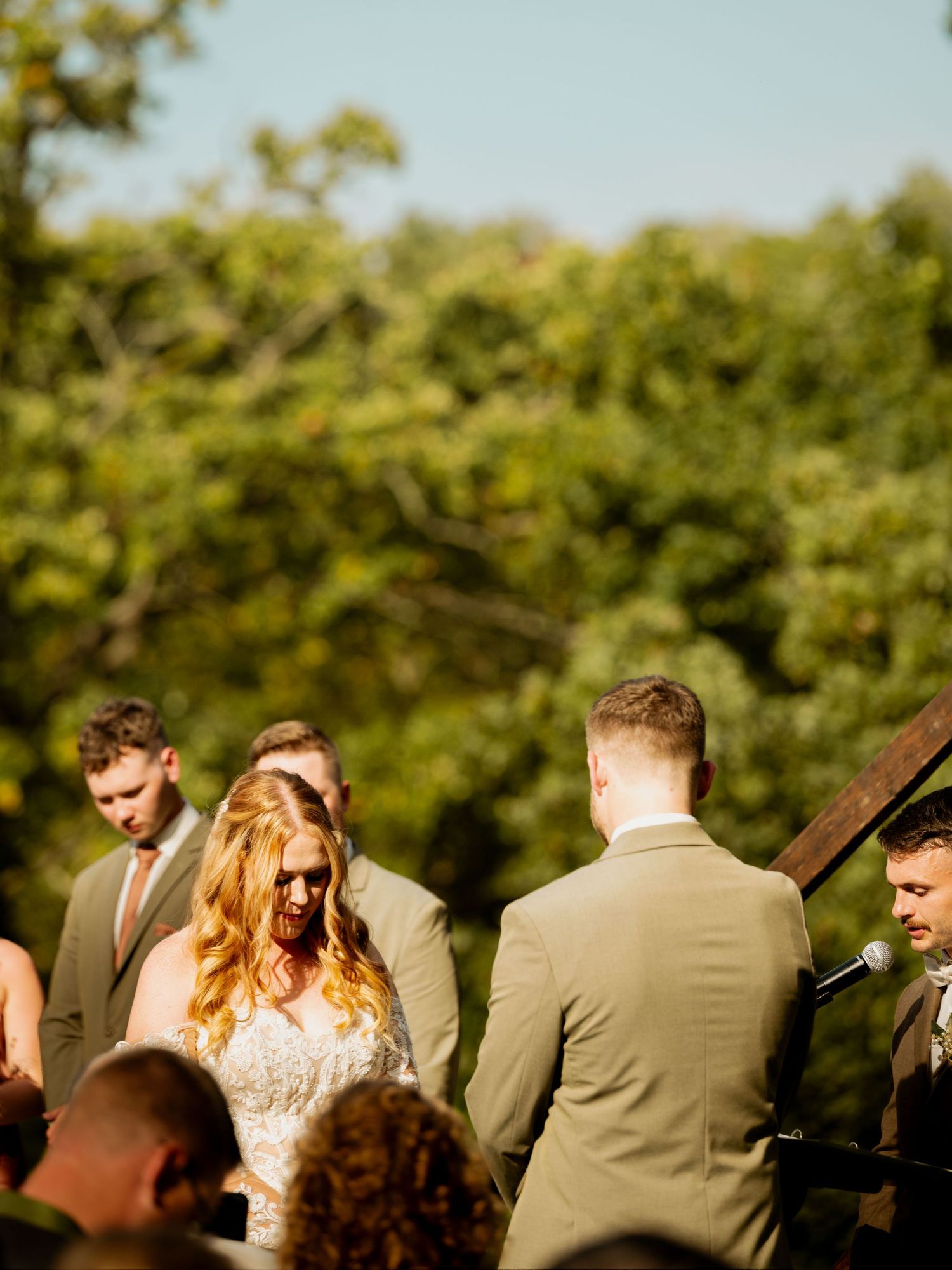 An outdoor wedding ceremony taking place in a sunlit forest setting.