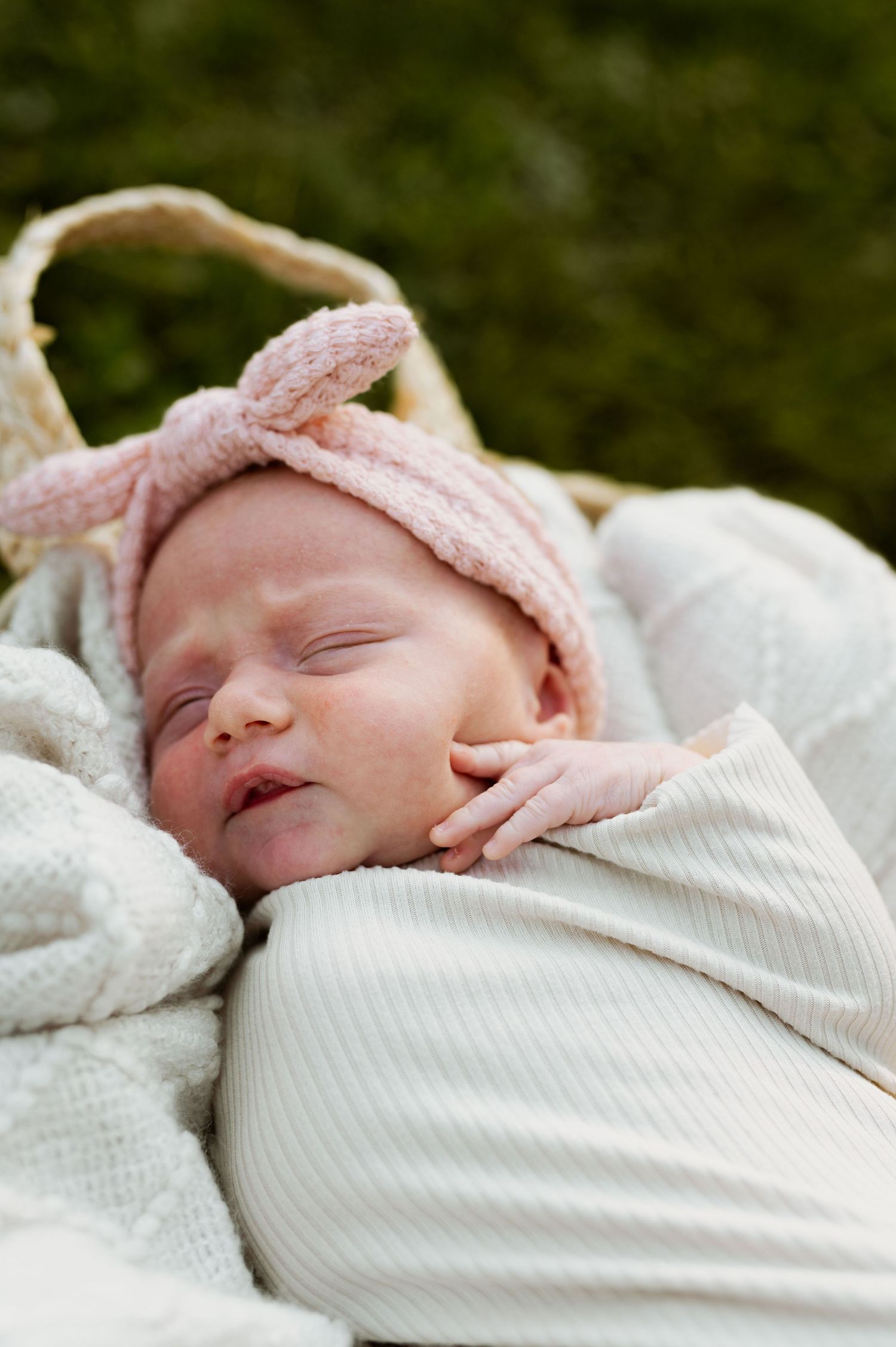 Sleeping newborn baby wrapped in white blanket with pink bow headband.