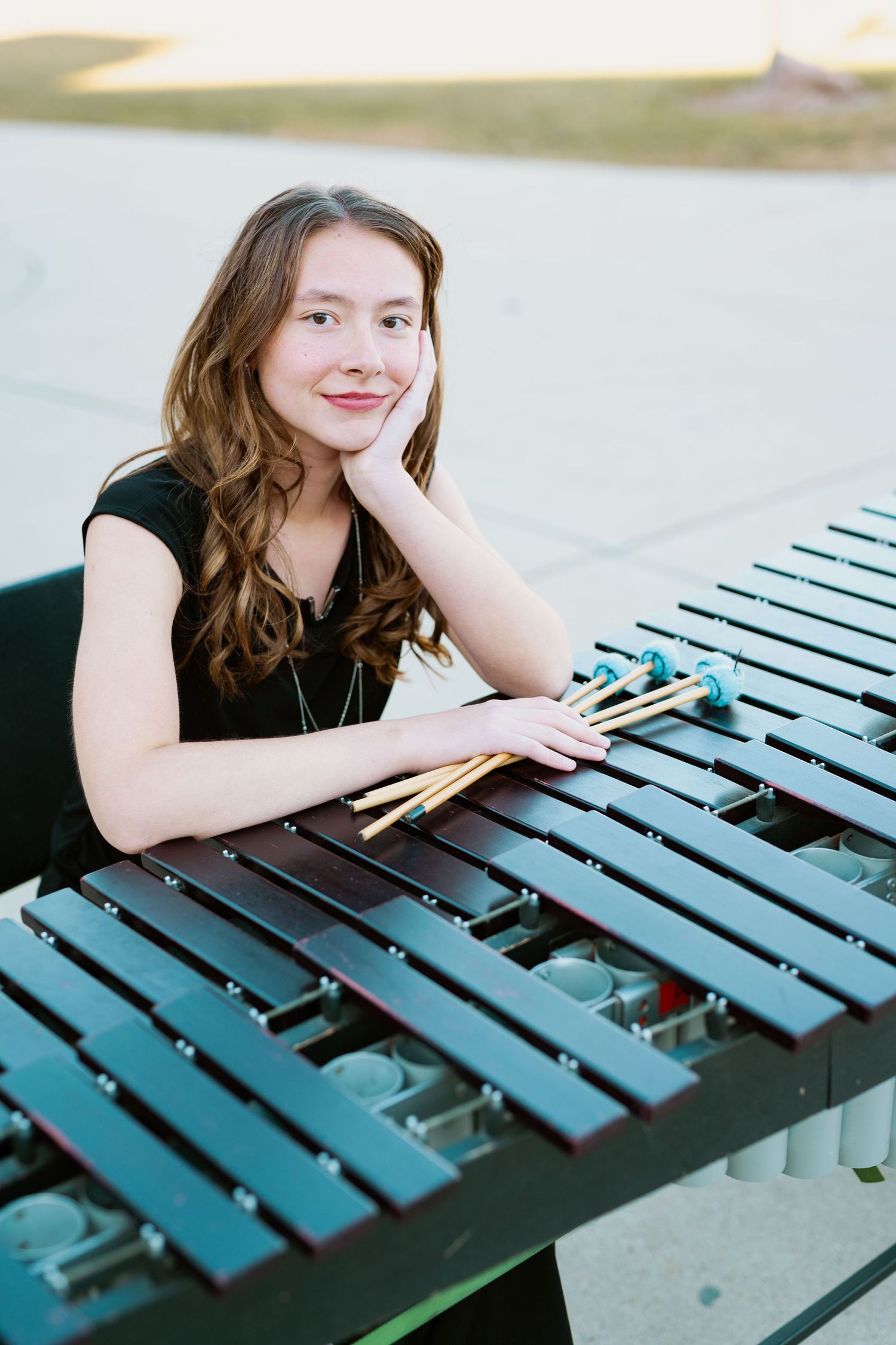 Student musician poses with drumsticks at outdoor vibraphone during band photoshoot.