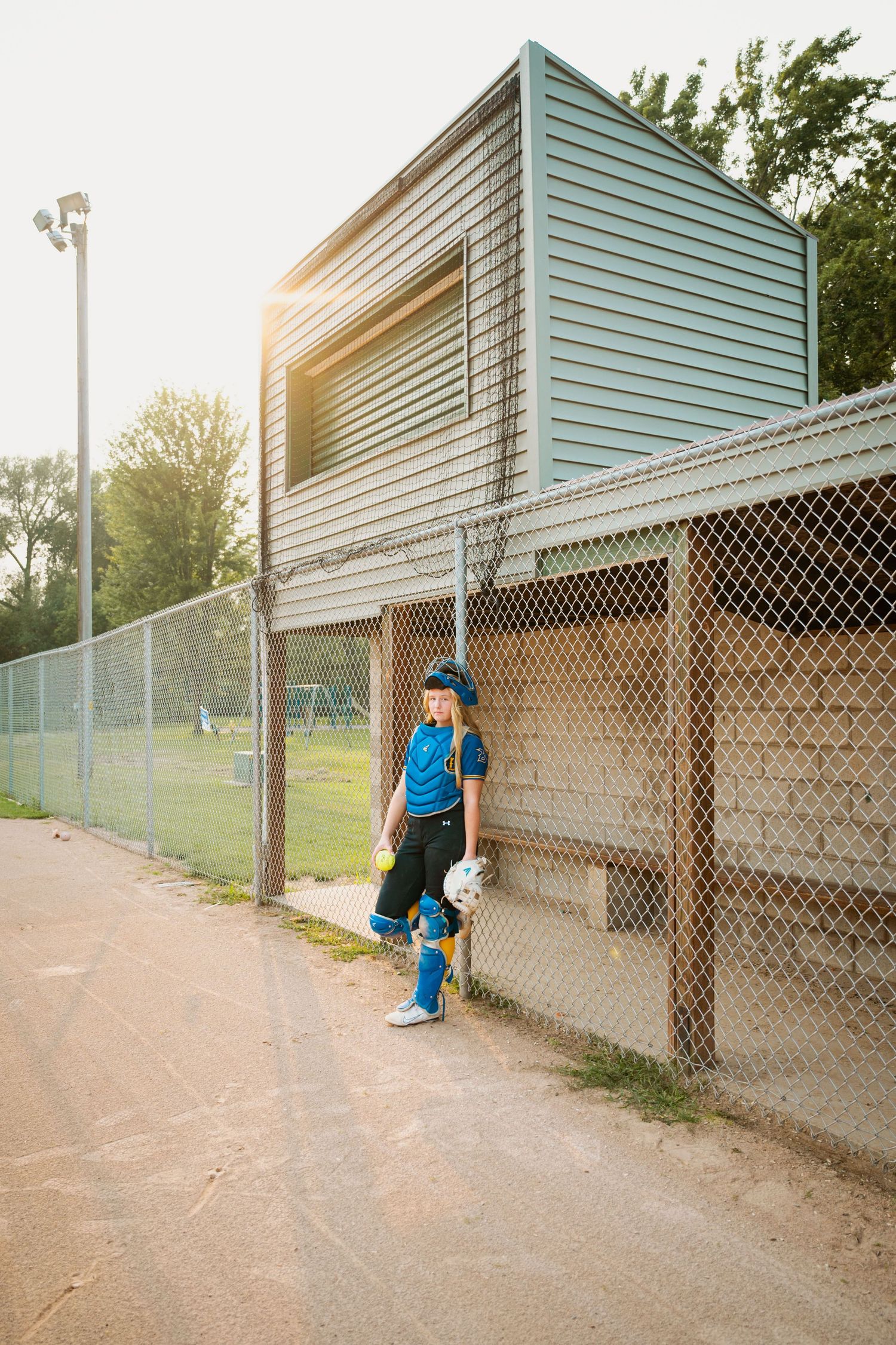 A series of panning shots showing a person in blue walking along a chain link fence at sunset.