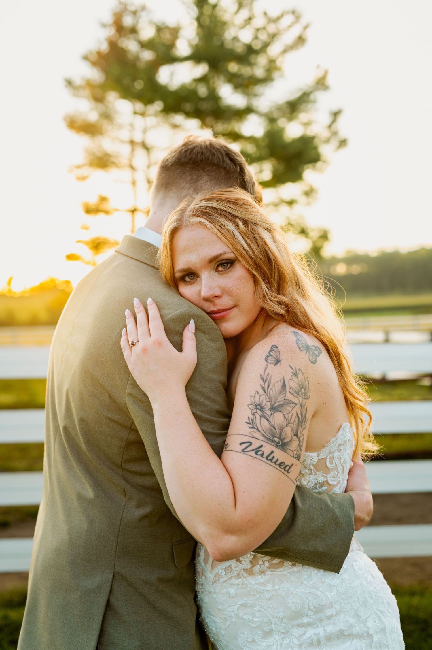 Intimate sunset wedding portraits showcase couple embracing by white fence.