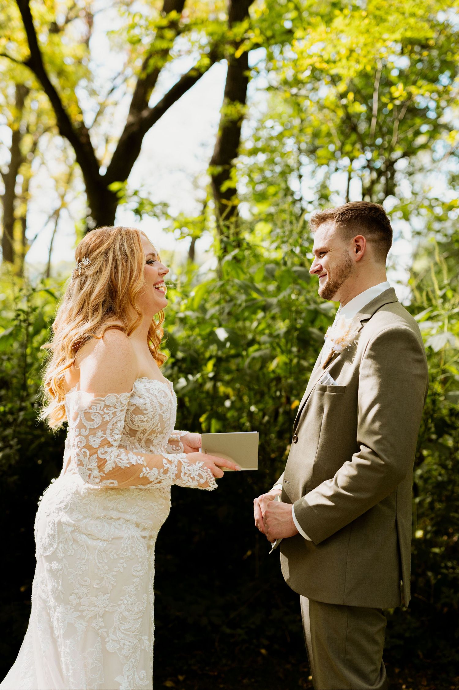 Couple sharing emotional reactions during their first look wedding moment in a sunlit wooded area.