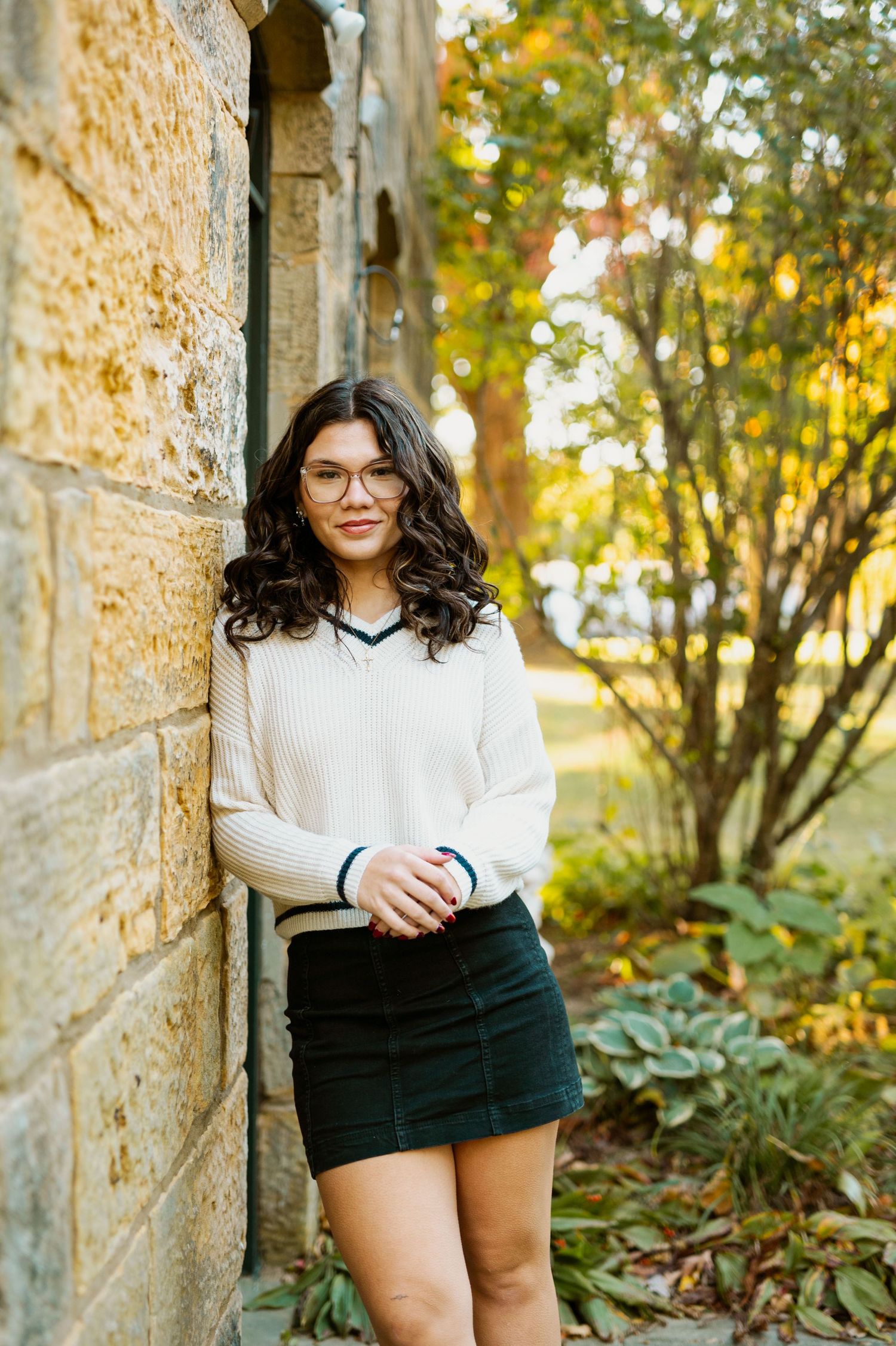 Casual outdoor portrait session against a stone wall with flowering bushes in natural lighting.