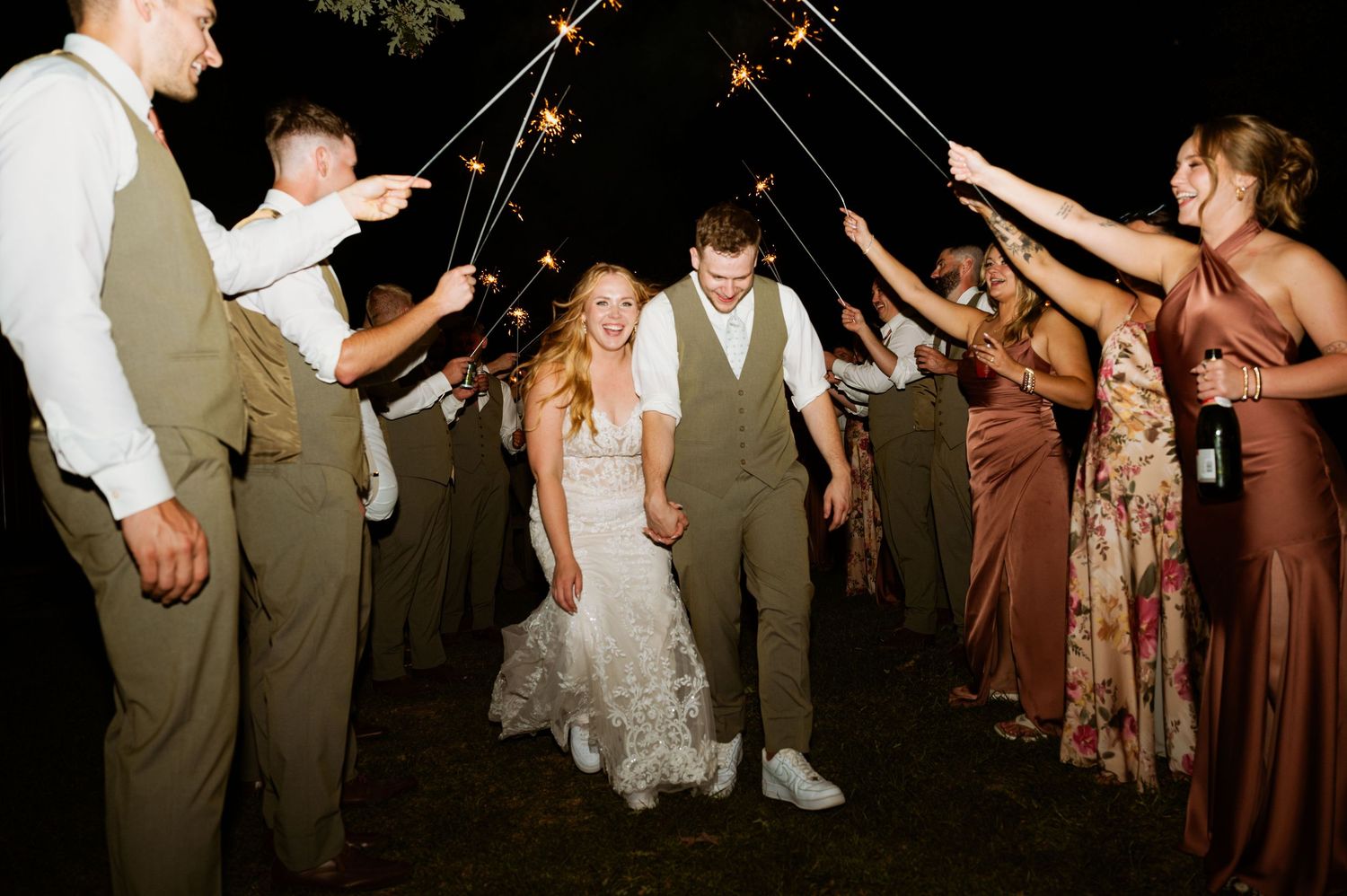 Wedding guests create a sparkler tunnel exit for the newlyweds during nighttime celebrations.