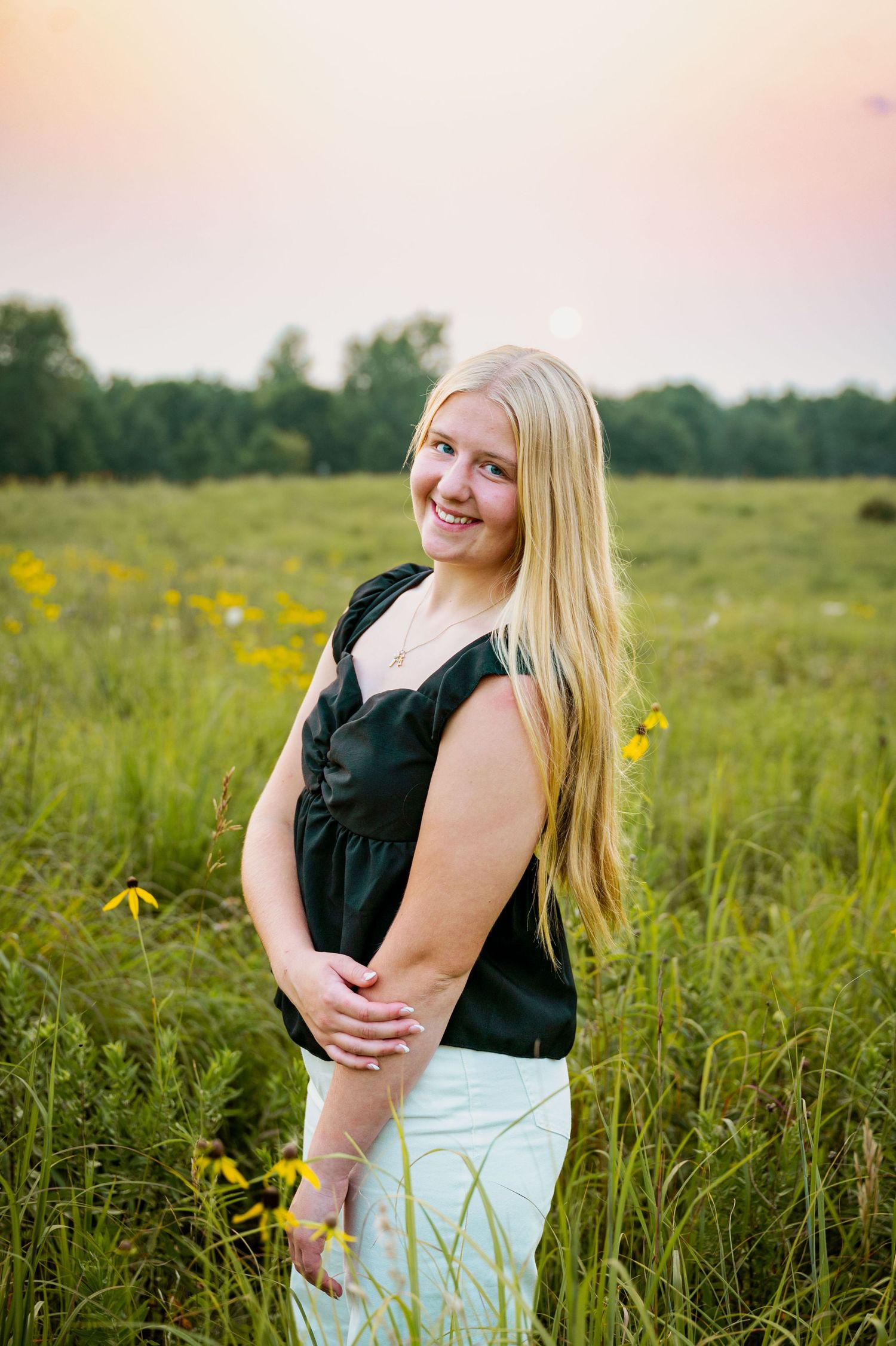 A person stands in a sunlit meadow filled with tall grass and yellow wildflowers during golden hour.