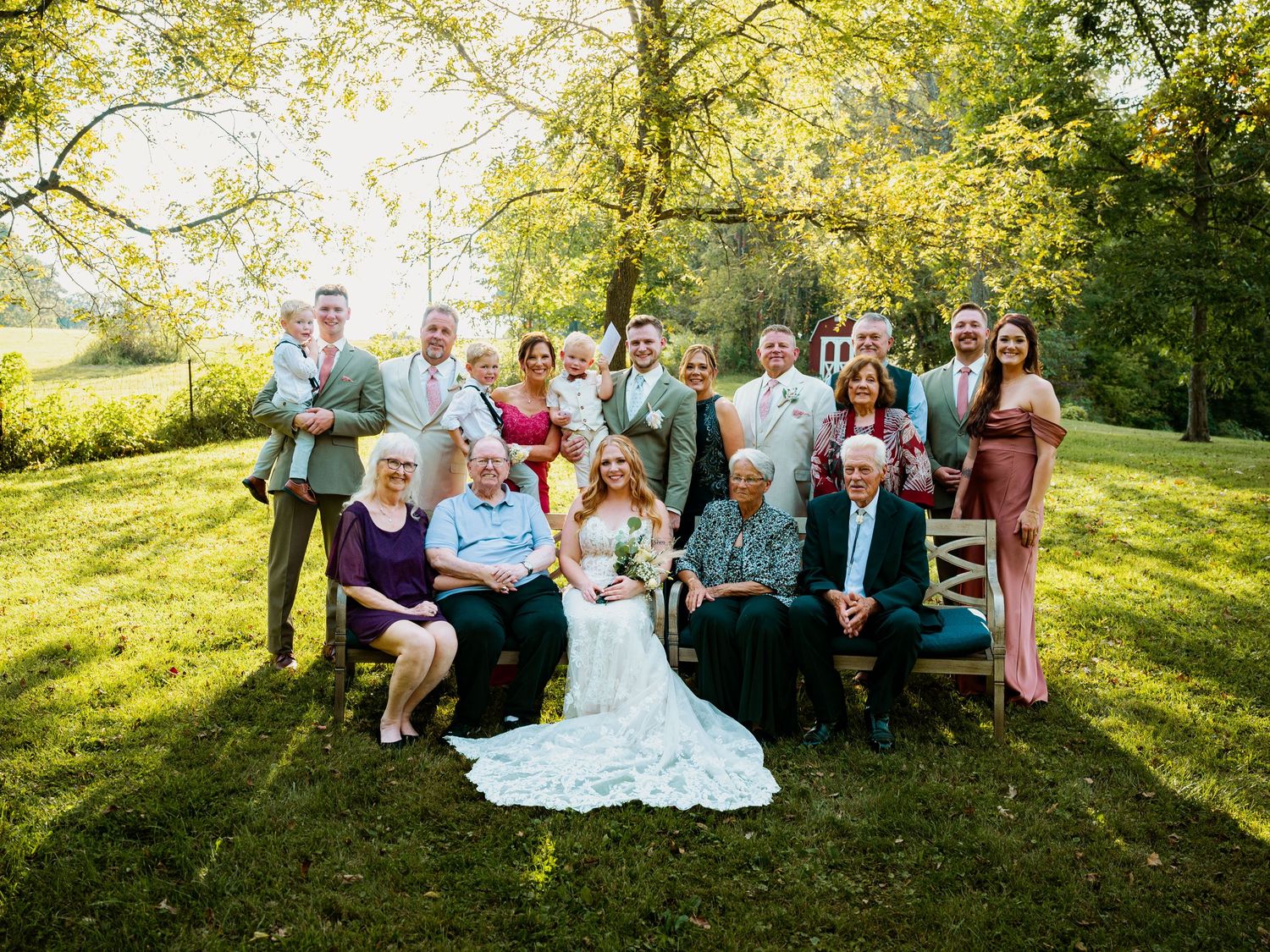 Wedding party and family portrait taken on a sunny lawn with natural greenery backdrop.
