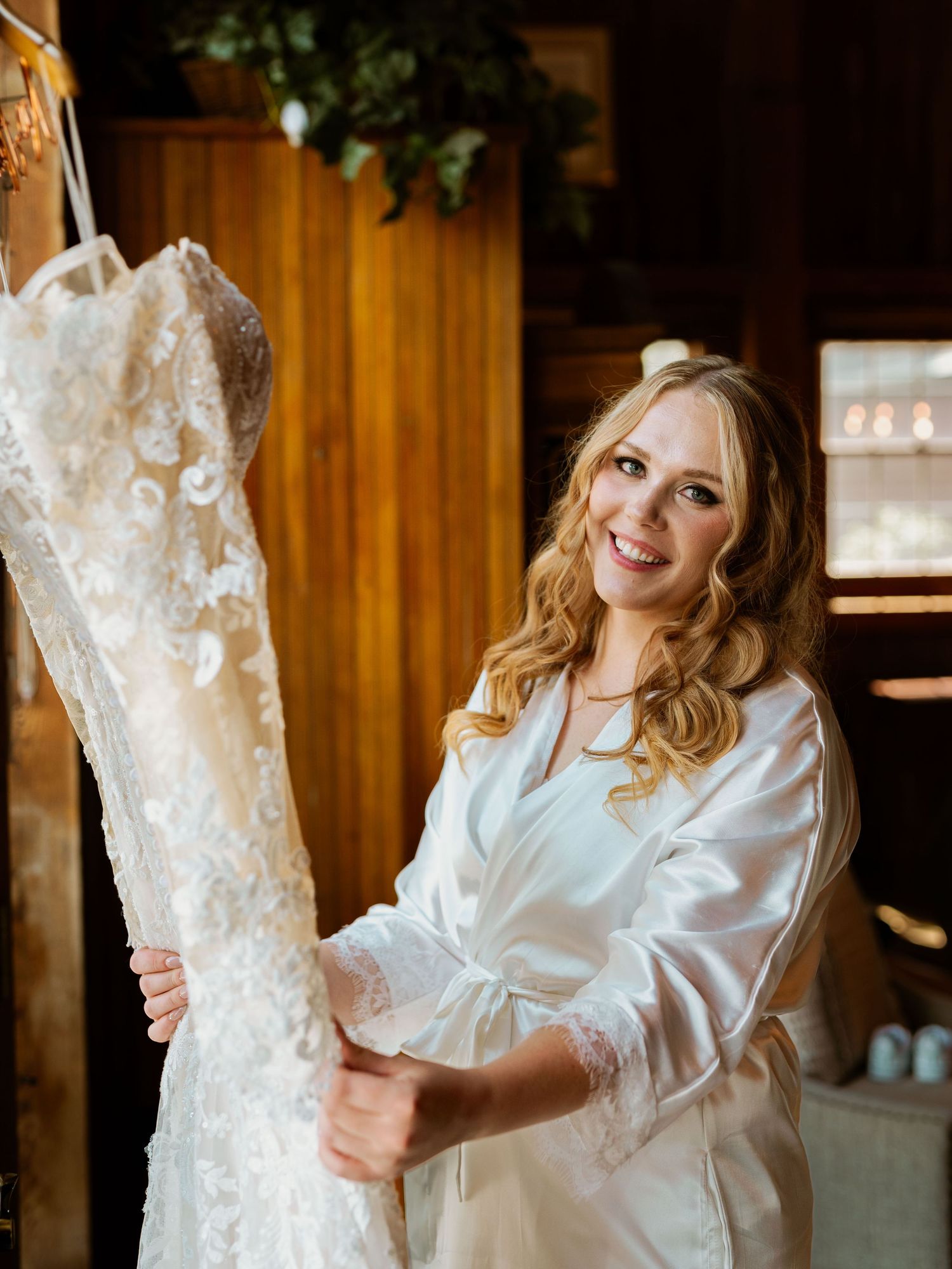 A lace wedding dress hangs while being prepared in a wooden-paneled dressing room.