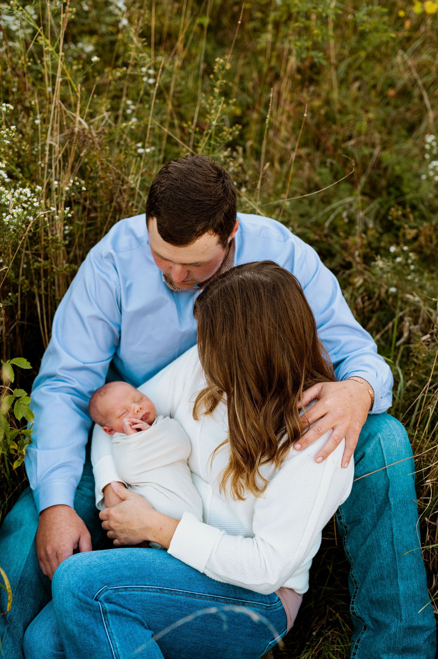 Romantic couple in casual attire embraces in a field of wildflowers during an outdoor photo session.