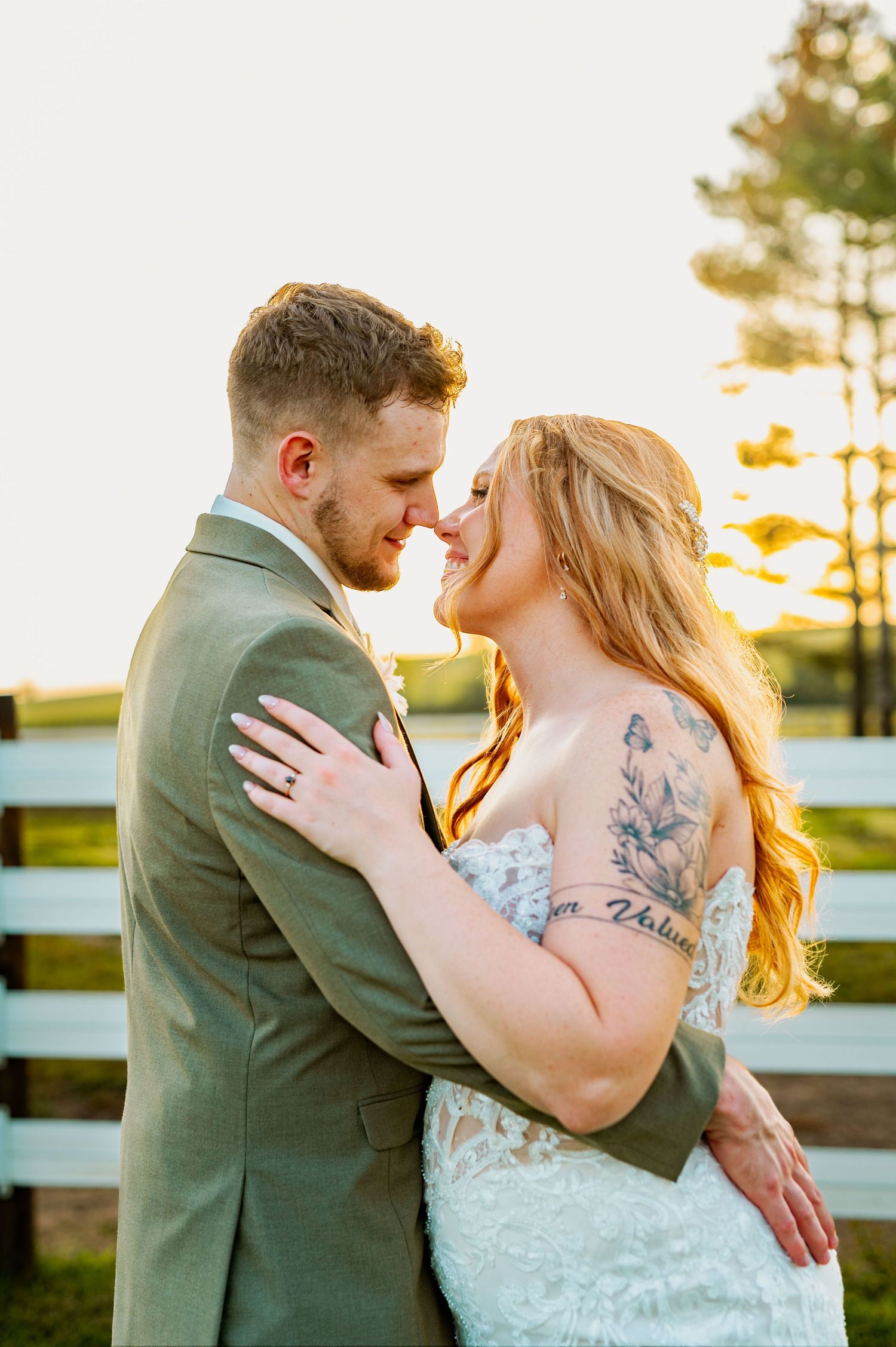 Romantic sunset wedding portrait with couple embracing against white fence backdrop.