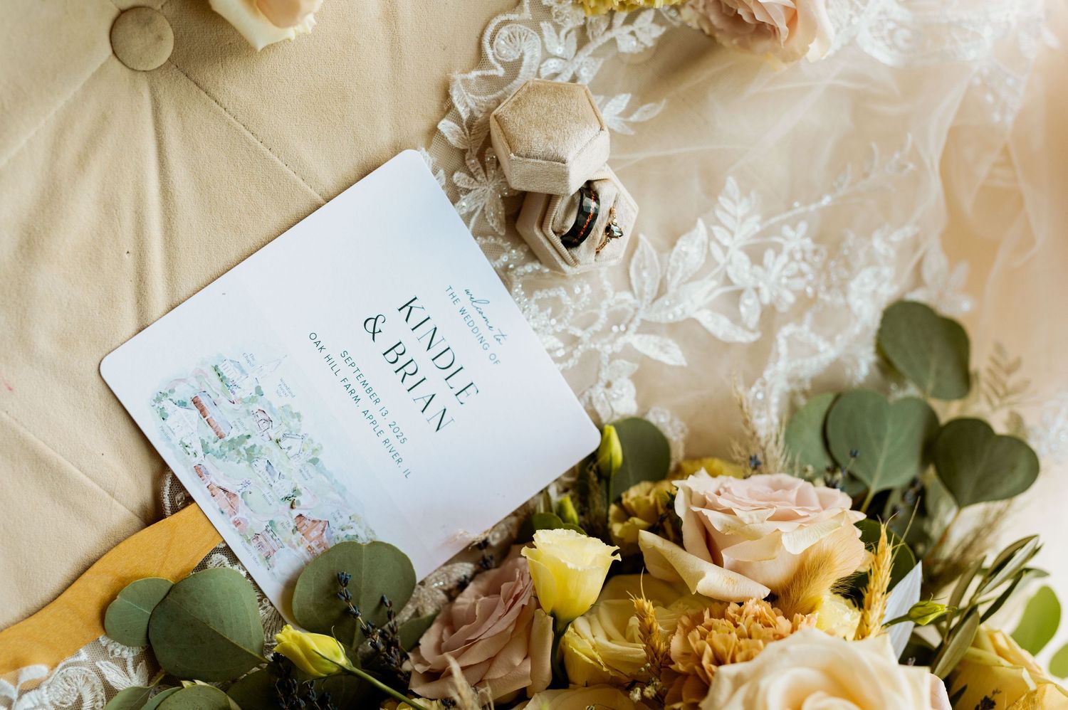 Wedding invitation suite with soft pink roses and eucalyptus leaves on cream-colored fabric.