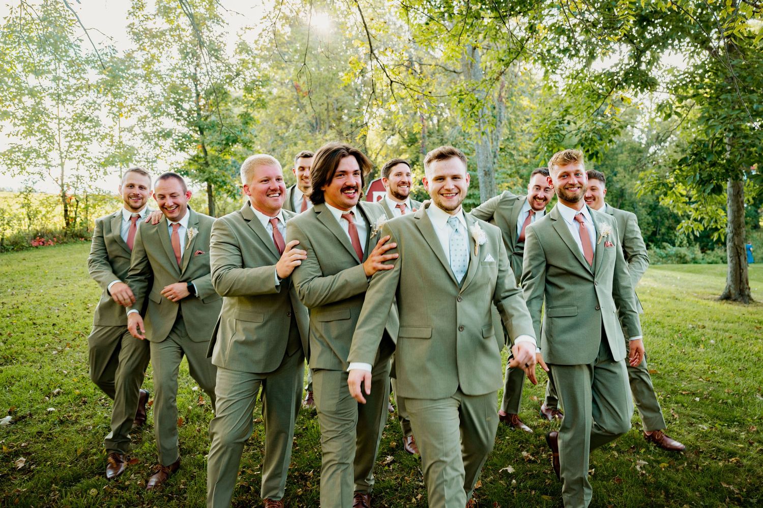 Groomsmen in sage green suits posing together outdoors for wedding party photos.