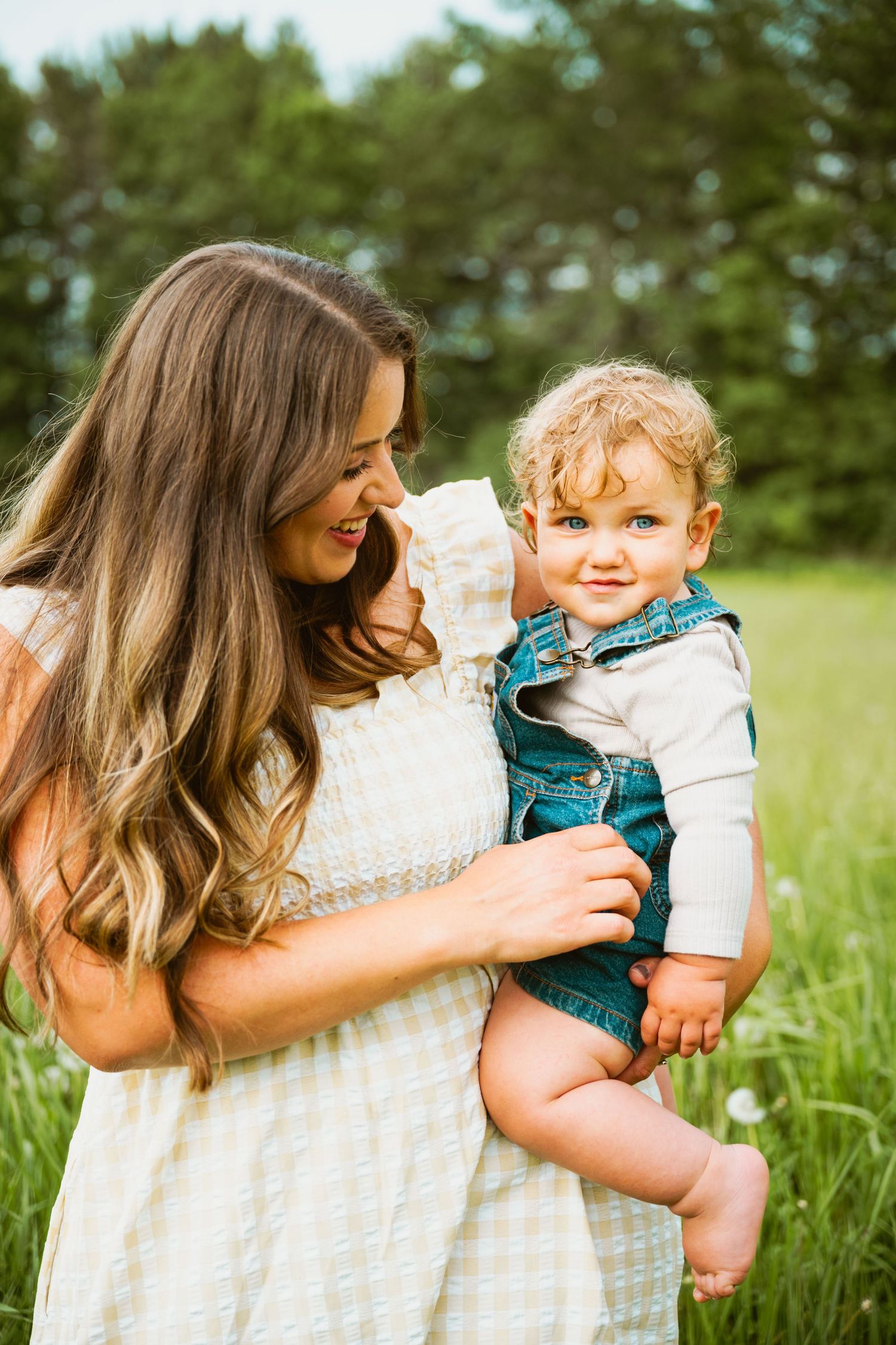 Mother and child share joyful embrace in sunny meadow wearing white and teal outfits.