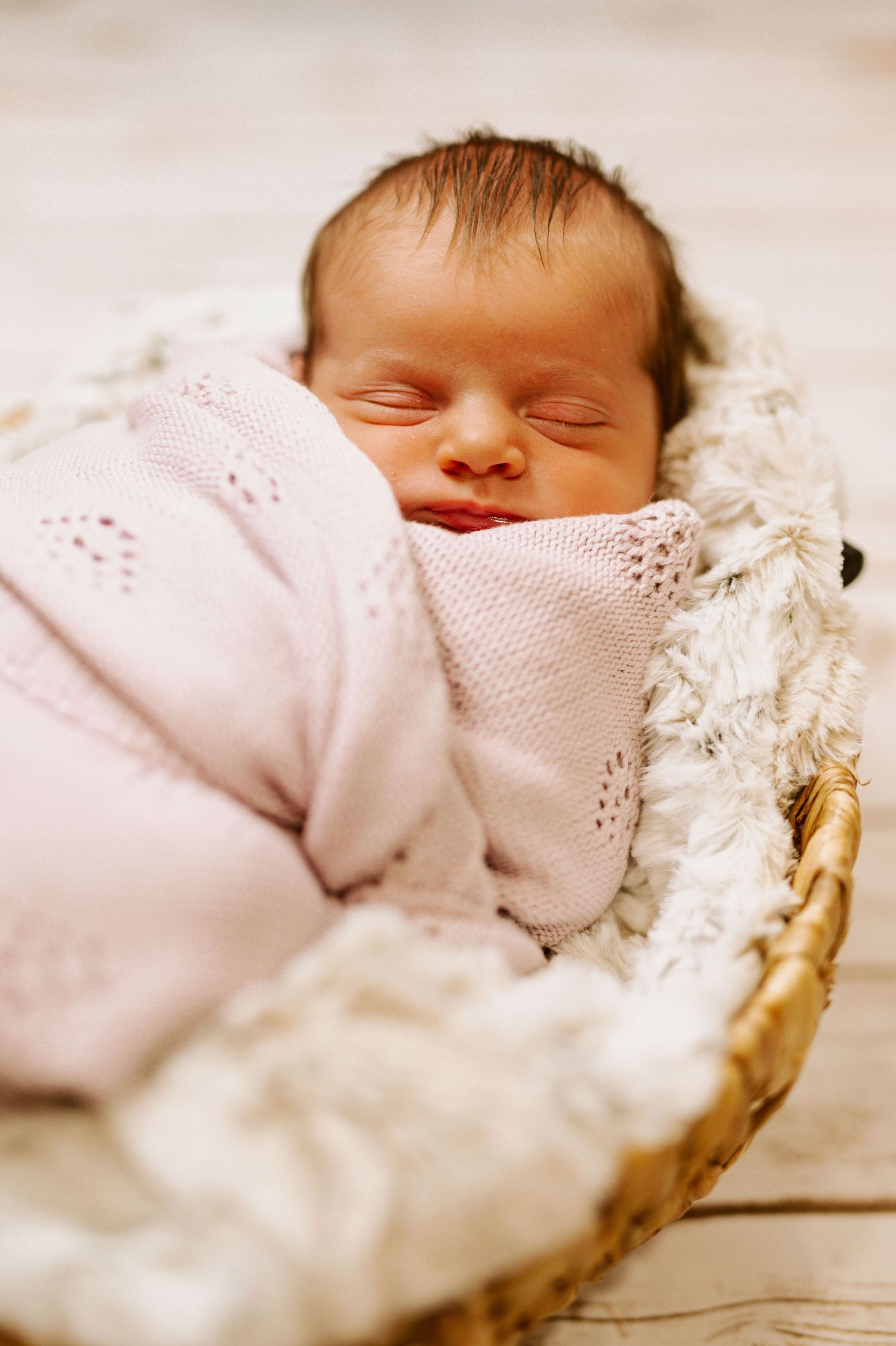 Peaceful newborn baby in pink knit outfit sleeping in white basket.