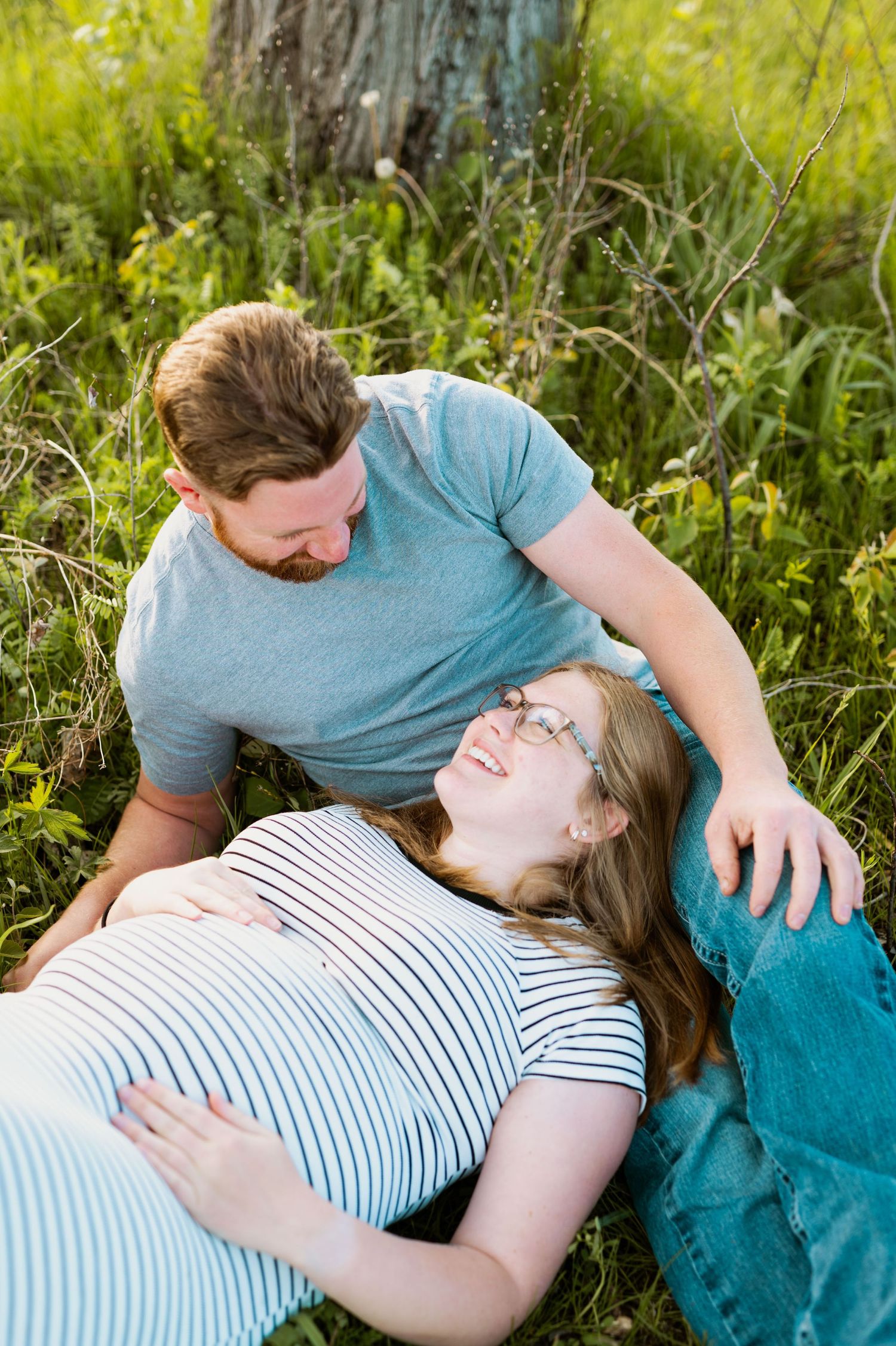 Expectant couple relaxing together in a sunny meadow with wildflowers.
