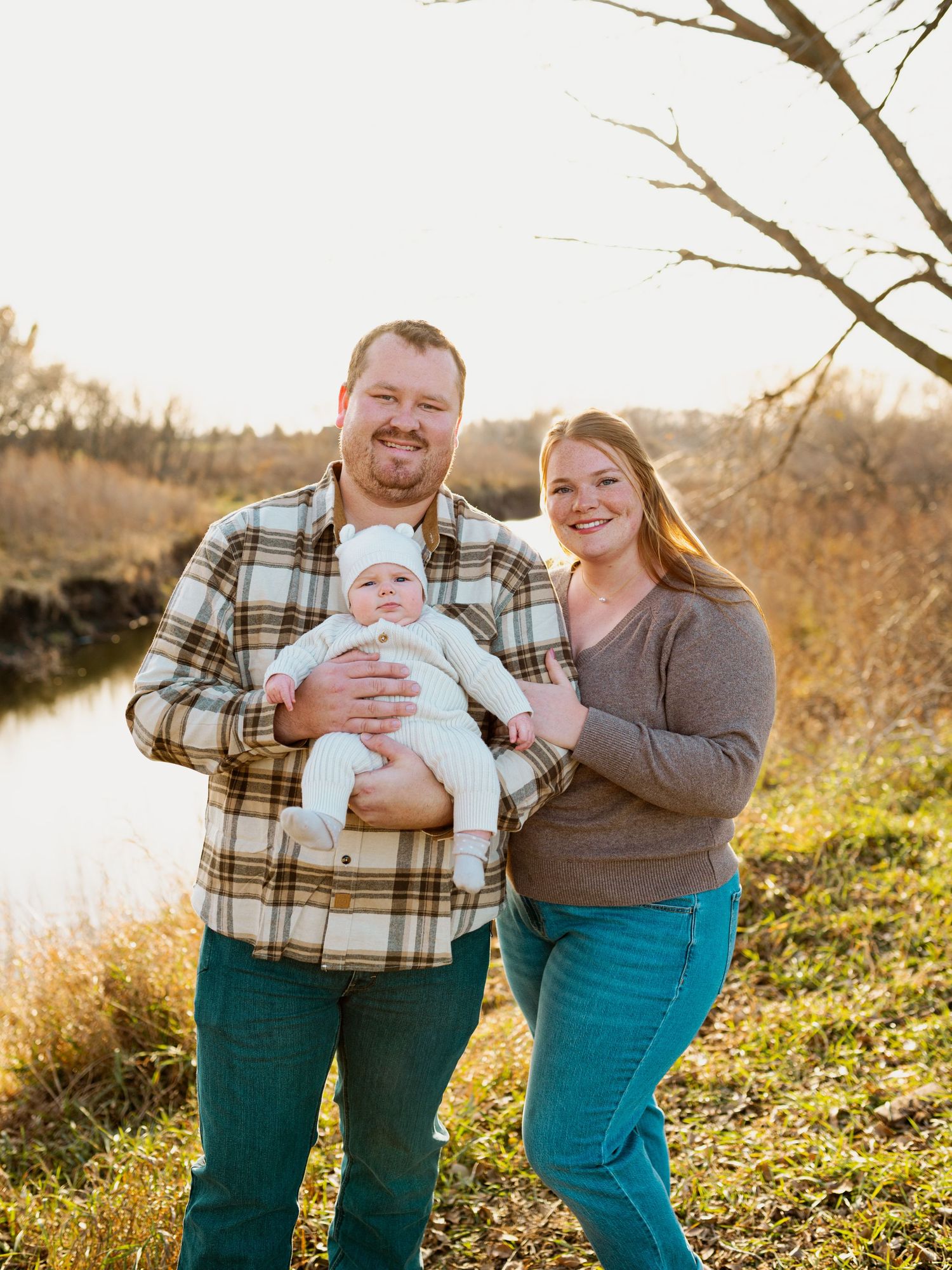 A family poses together in a field at sunset wearing coordinating brown and green outfits during an outdoor photo session.
