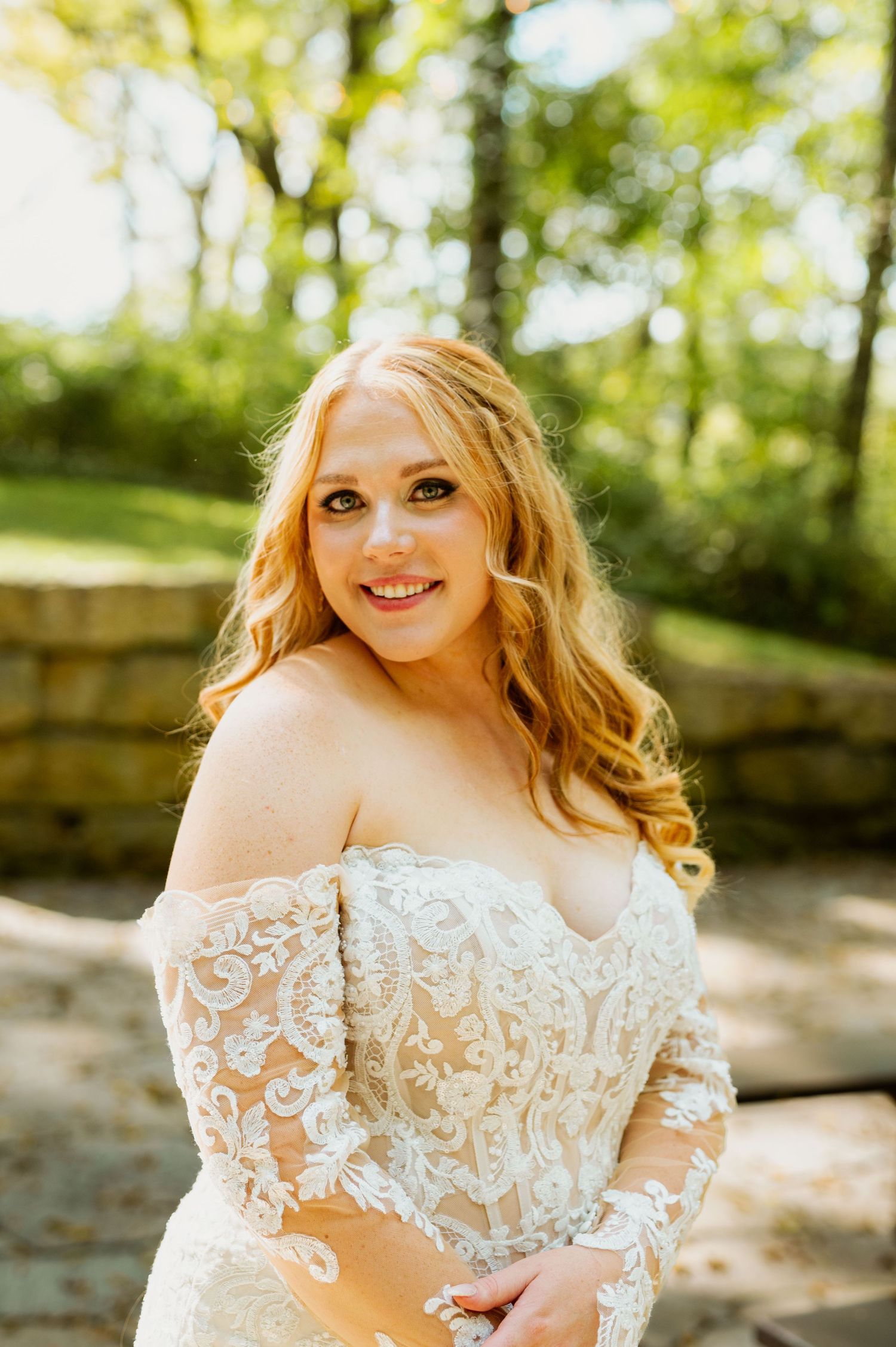 An elegant lace wedding gown with off-shoulder sleeves photographed in natural outdoor lighting.