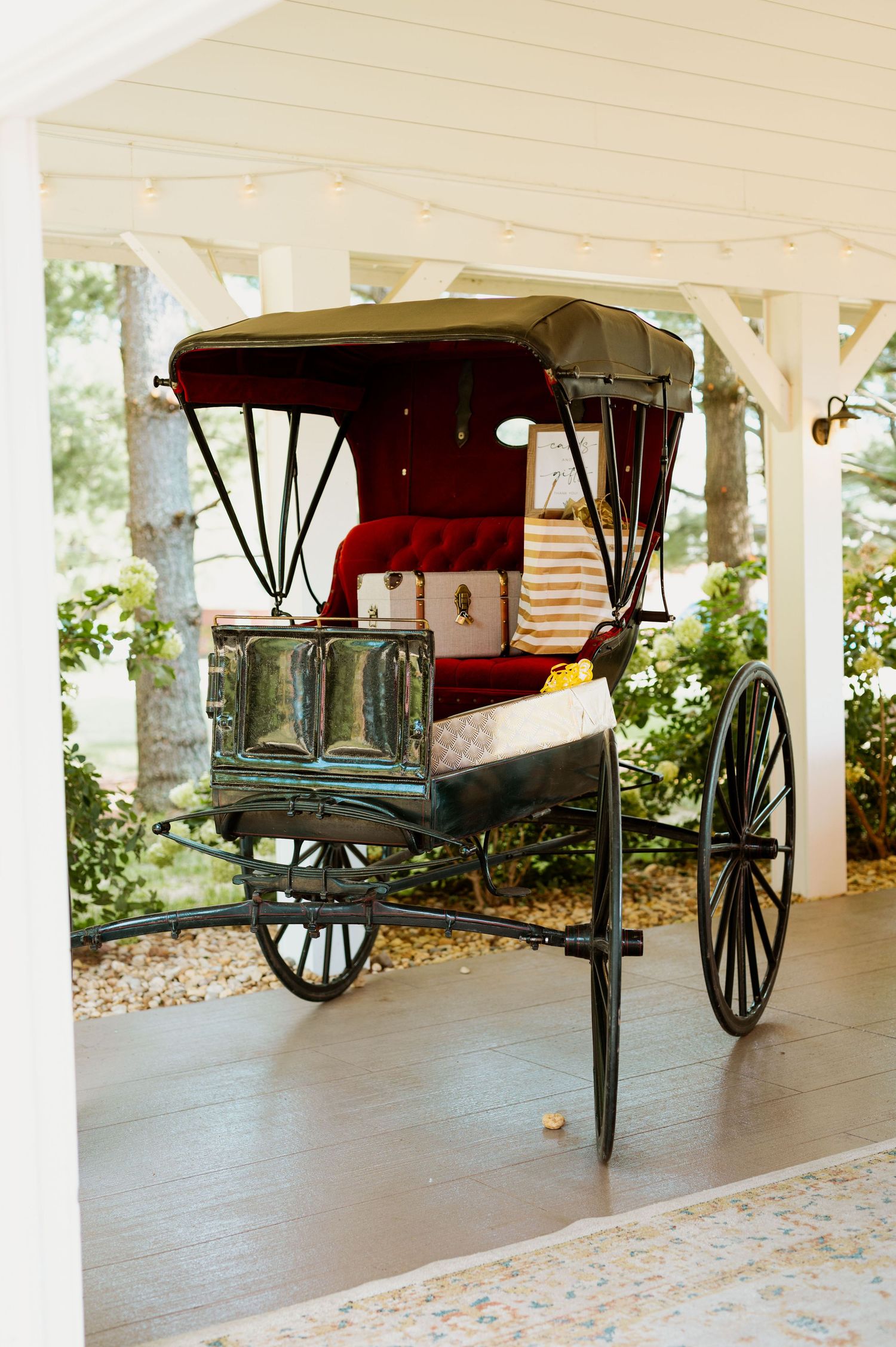 Vintage horse-drawn carriage displayed under a covered porch area with white columns.