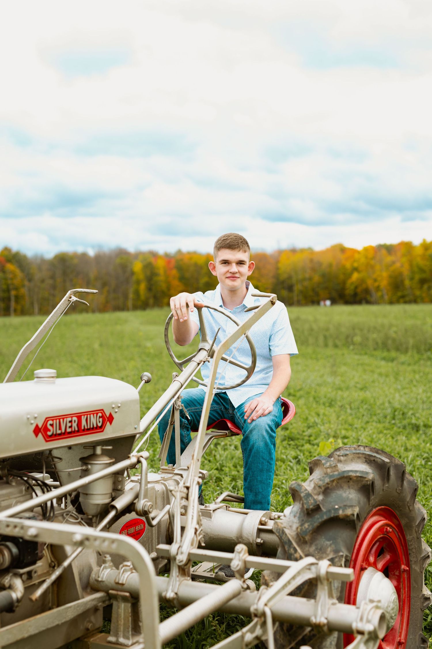 Person sitting on a vintage Silver King tractor in a sunny field with autumn trees in background.