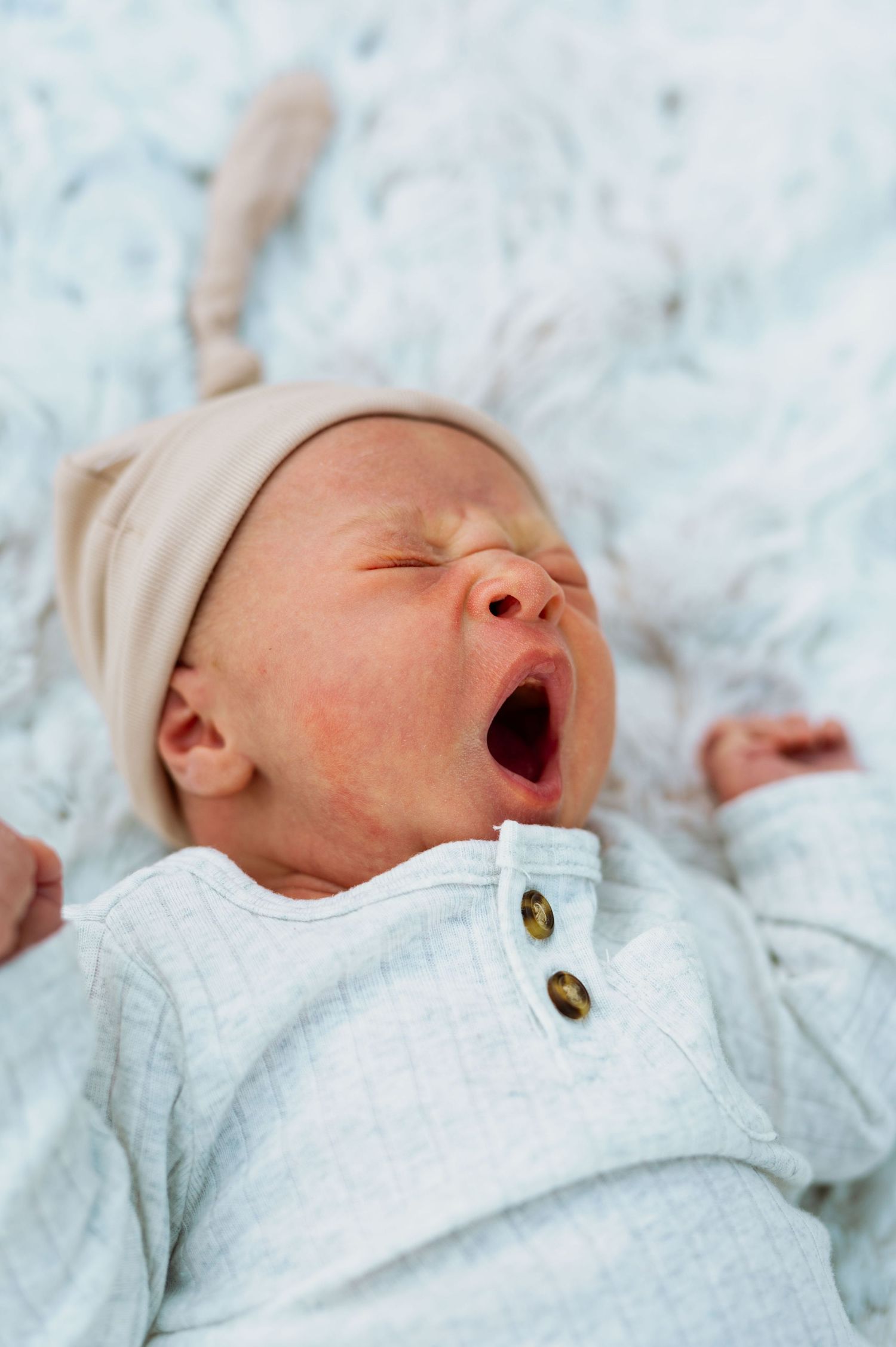 Sleeping newborn in white outfit yawning during photo session.