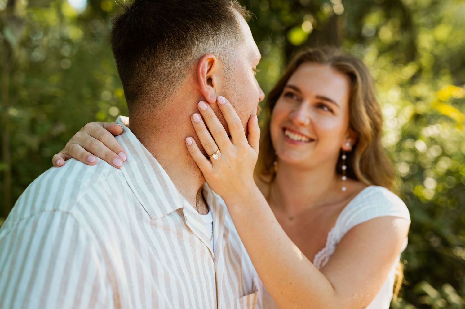 A tender moment captured between a couple with golden sunlight filtering through trees.