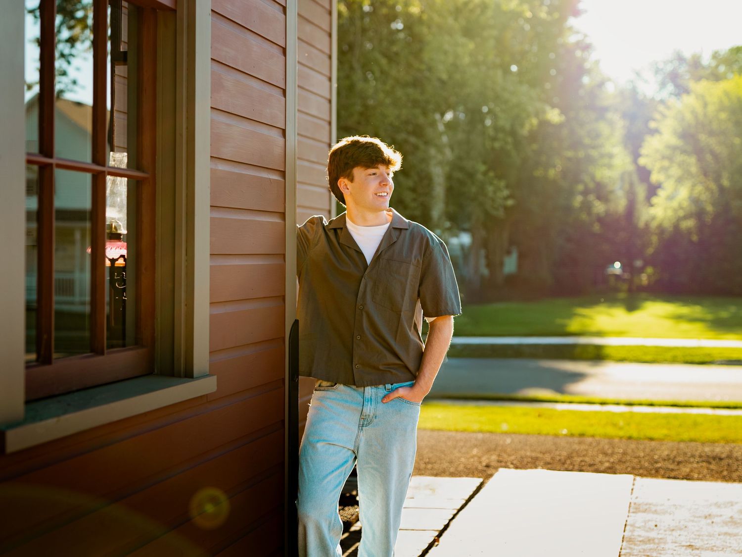 A person in casual attire walks down a sunlit pathway near a building with warm evening light filtering through trees.