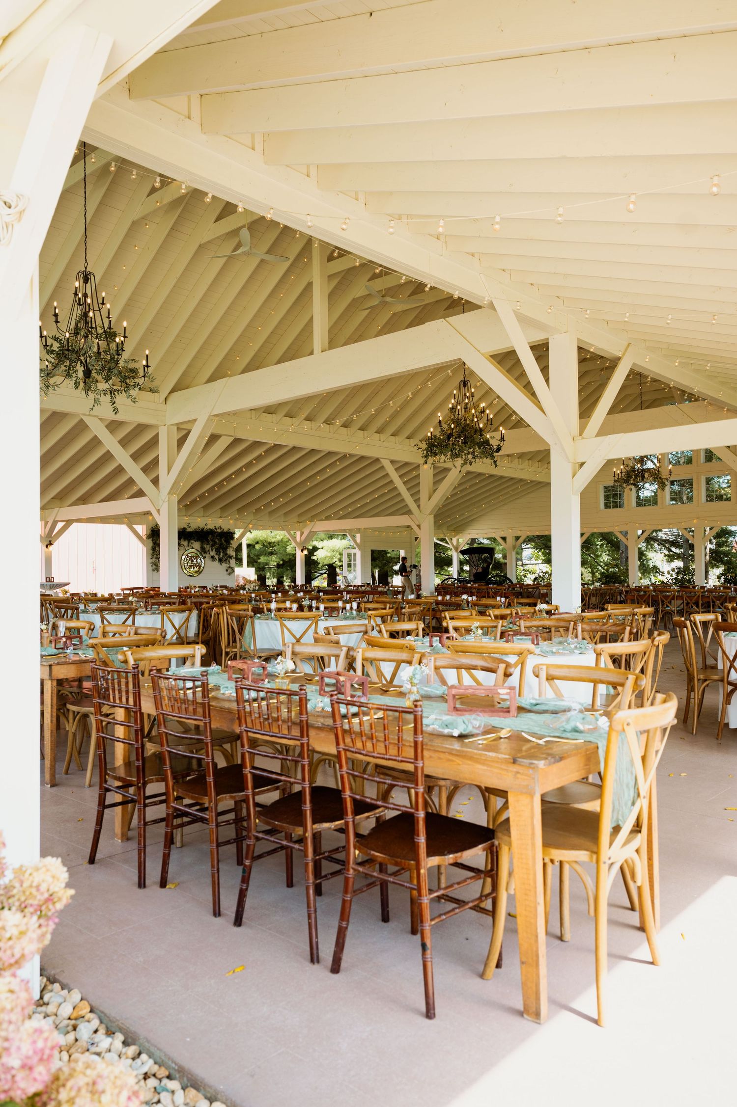 Large wedding reception venue with wooden tables and chairs set up under white vaulted ceilings.